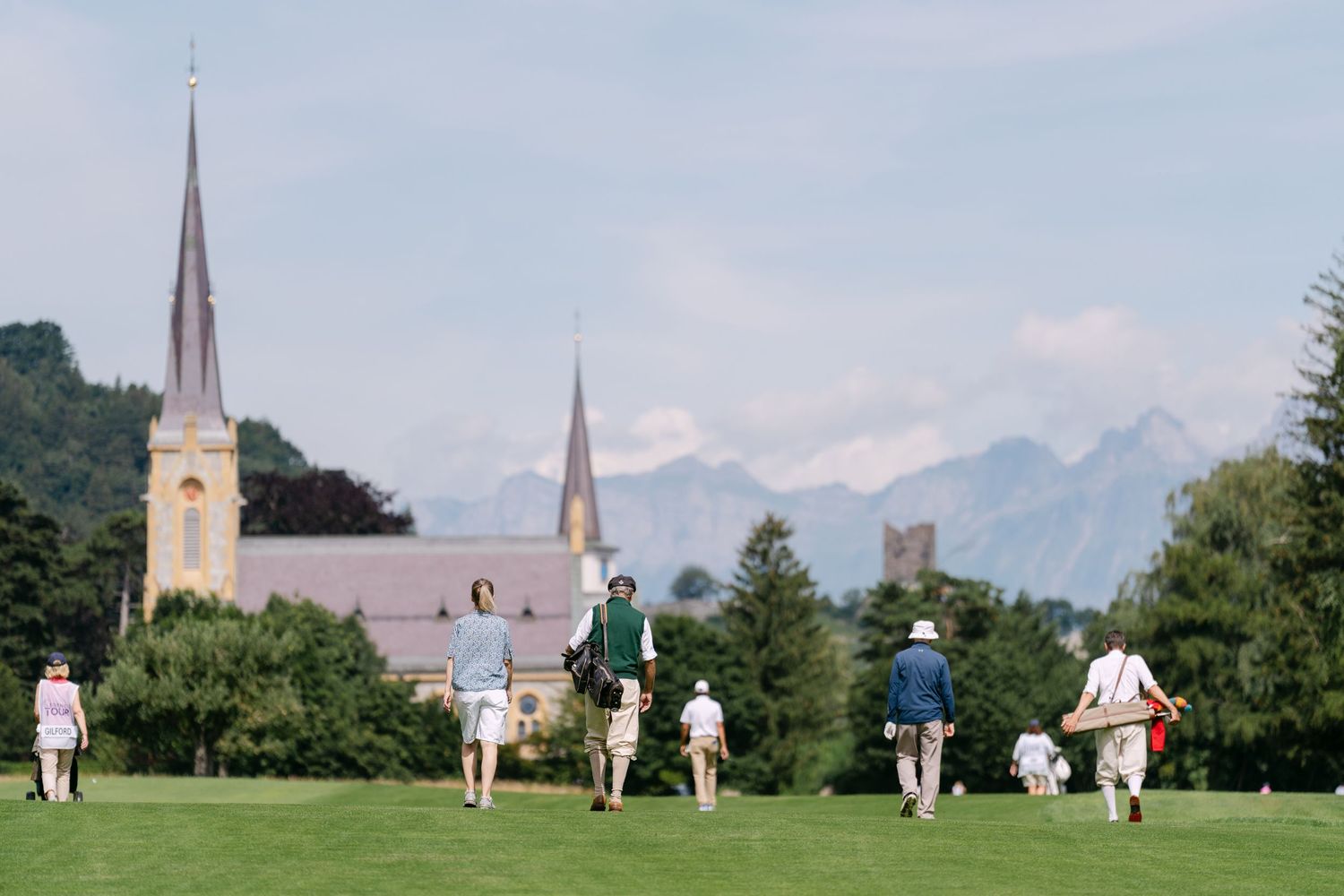 Golf course landscape with church spires visible in the background against a blue sky.