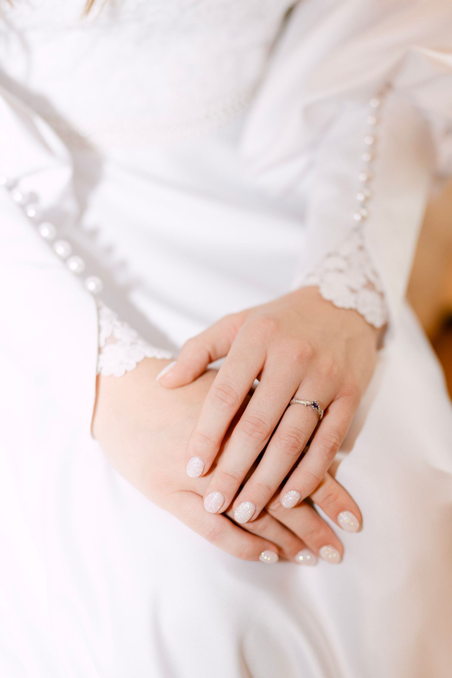 Close-up of hands wearing delicate jewelry against white fabric.