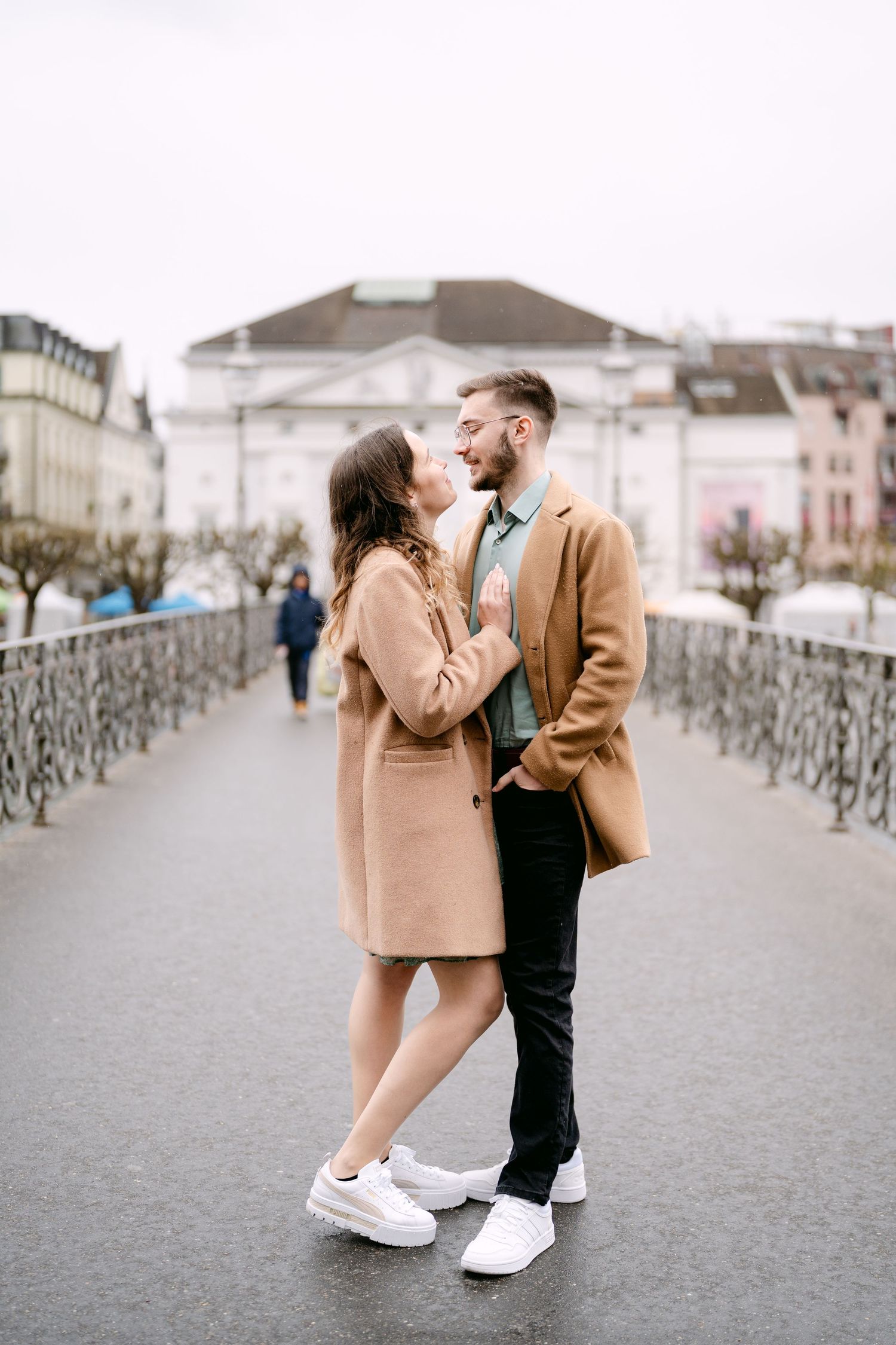 A couple shares an intimate moment on a bridge wearing coordinated camel and black outfits.