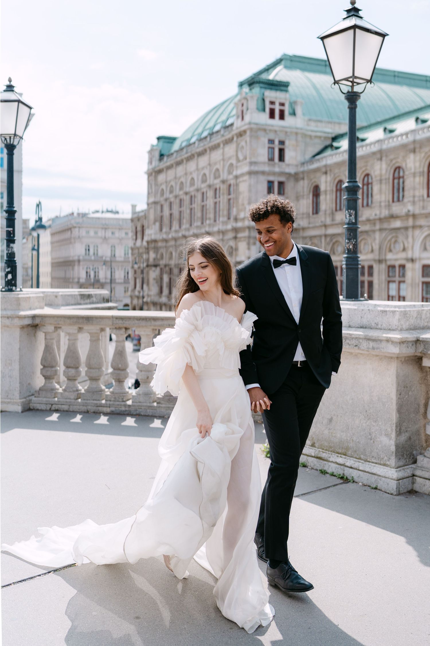 Wedding couple dances playfully on grand marble terrace with historic architecture backdrop.