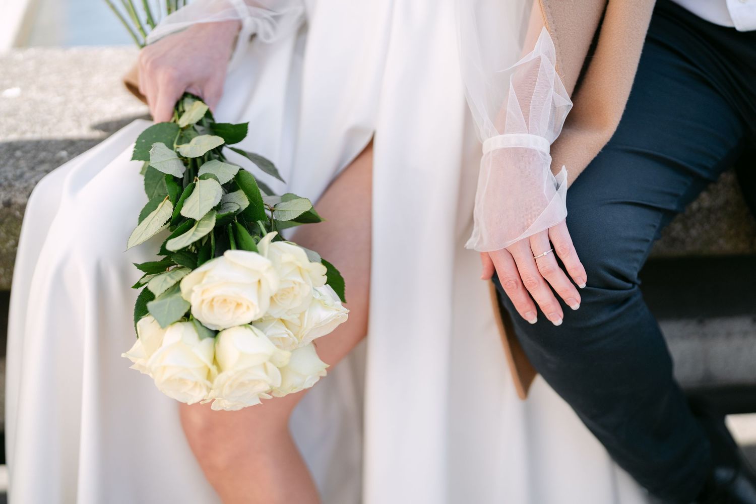 Closeup details of white roses and flowing wedding dress fabric against urban backdrop.