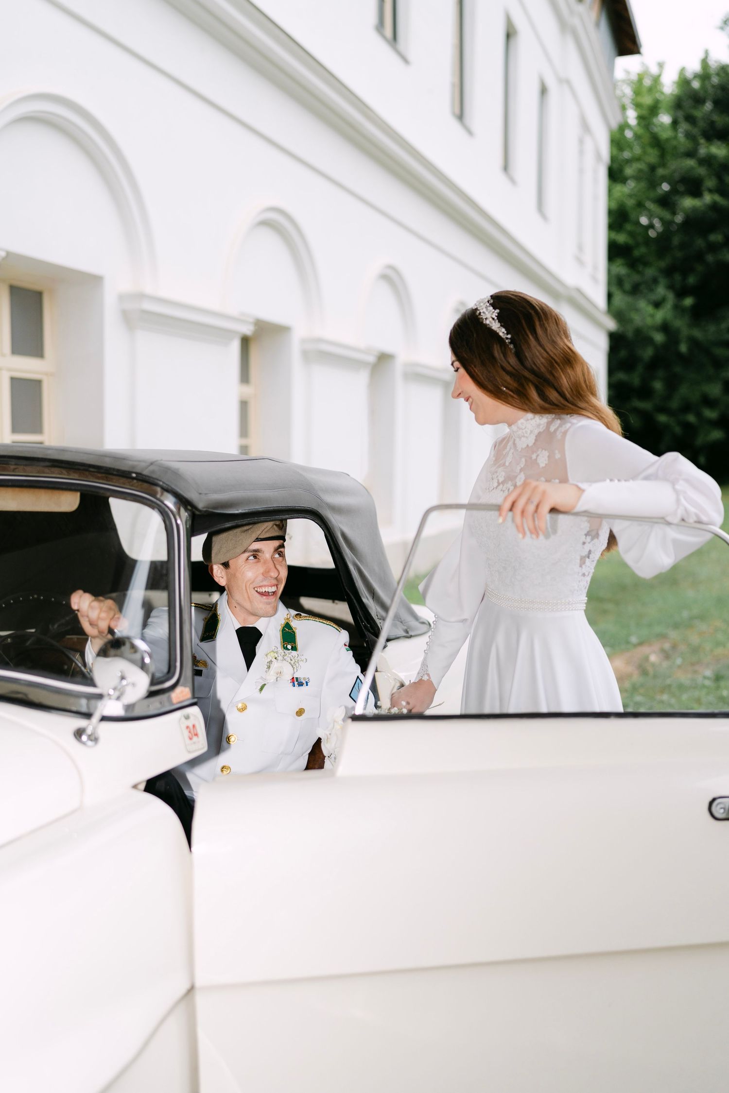 A white vintage car parked in front of a white building with arched architecture.