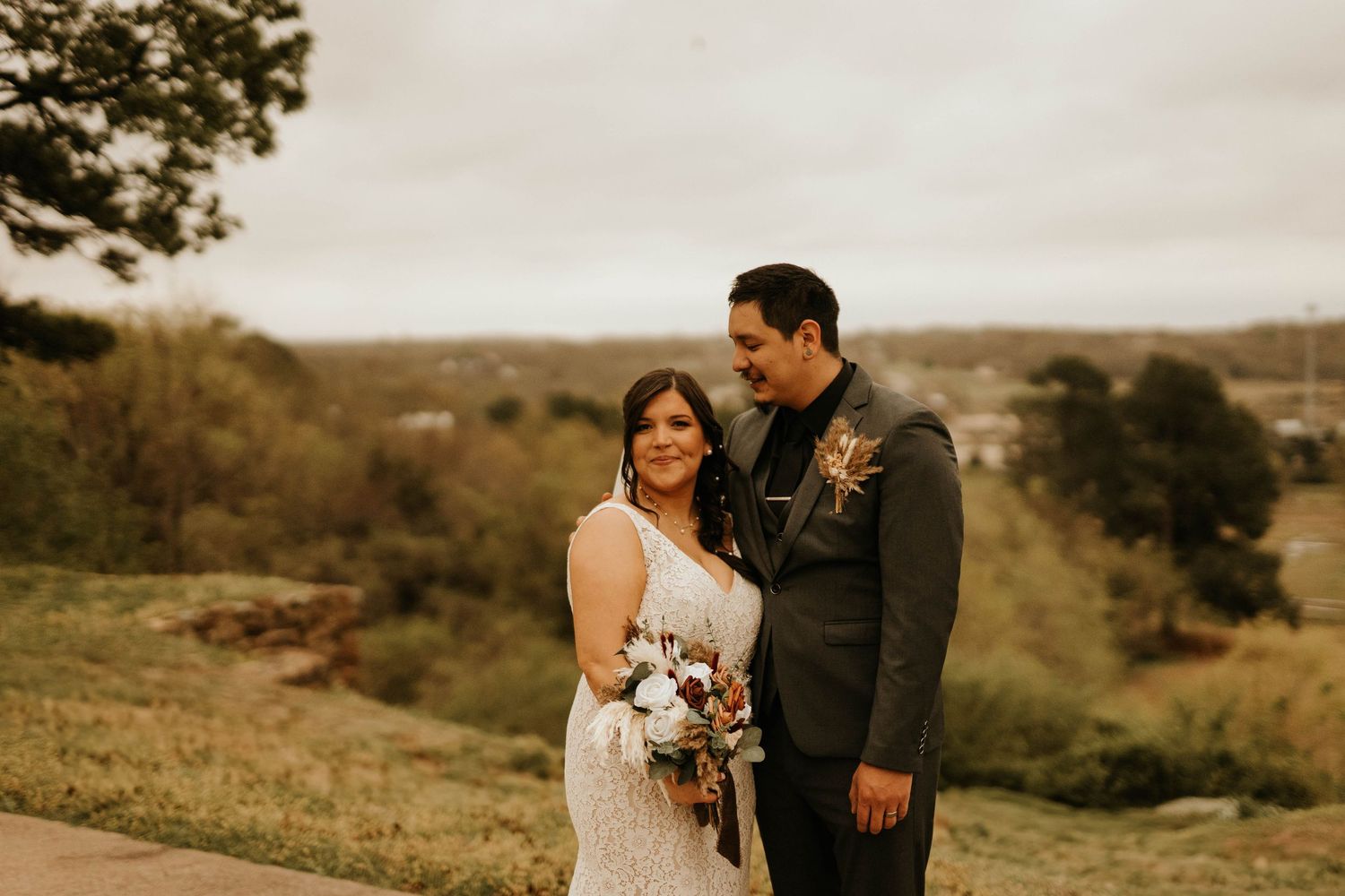 Couple shares tender moment on hilltop overlooking scenic landscape in wedding attire.