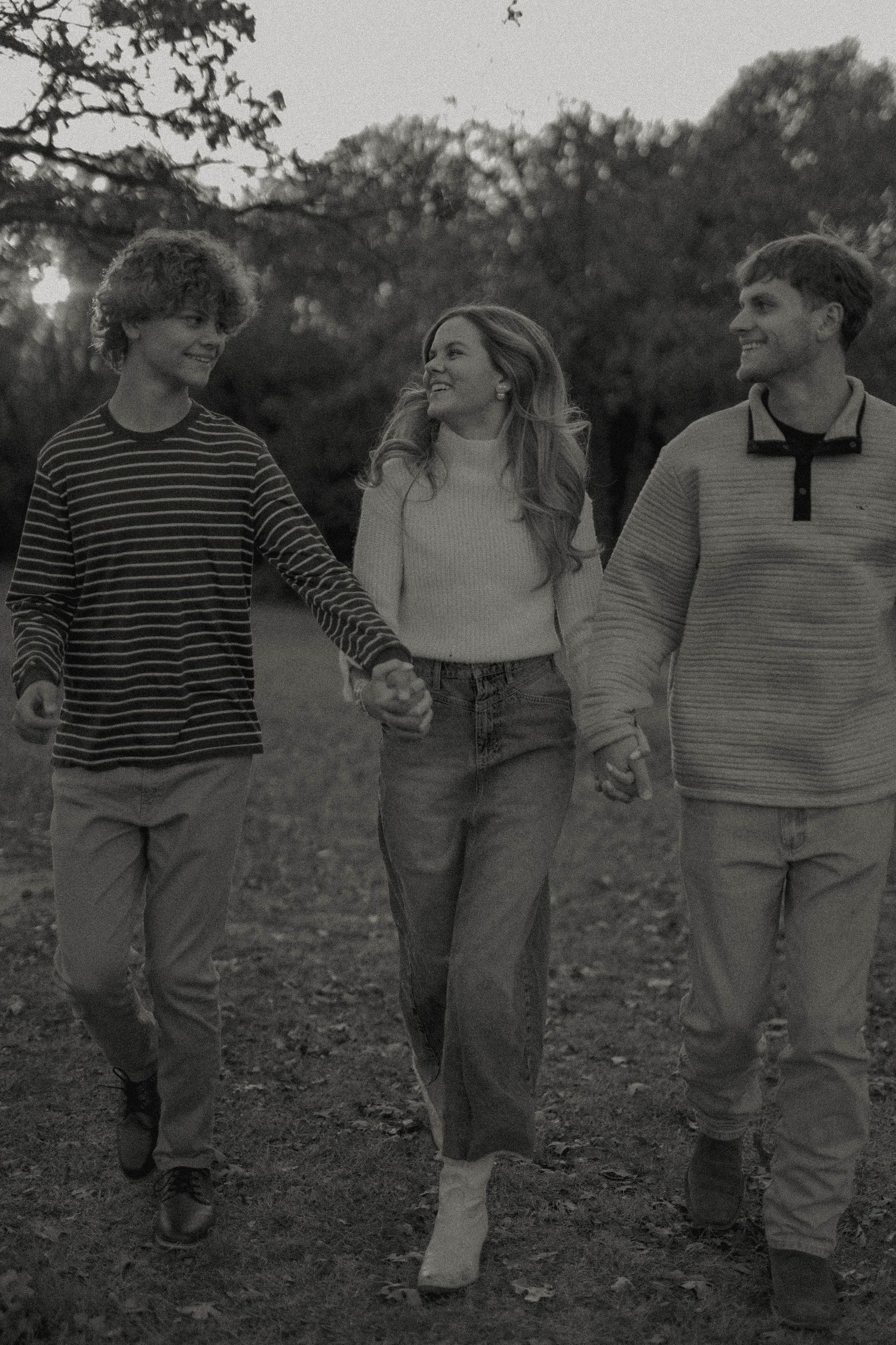 Friends walking and laughing together on wooded path at dusk in casual attire.