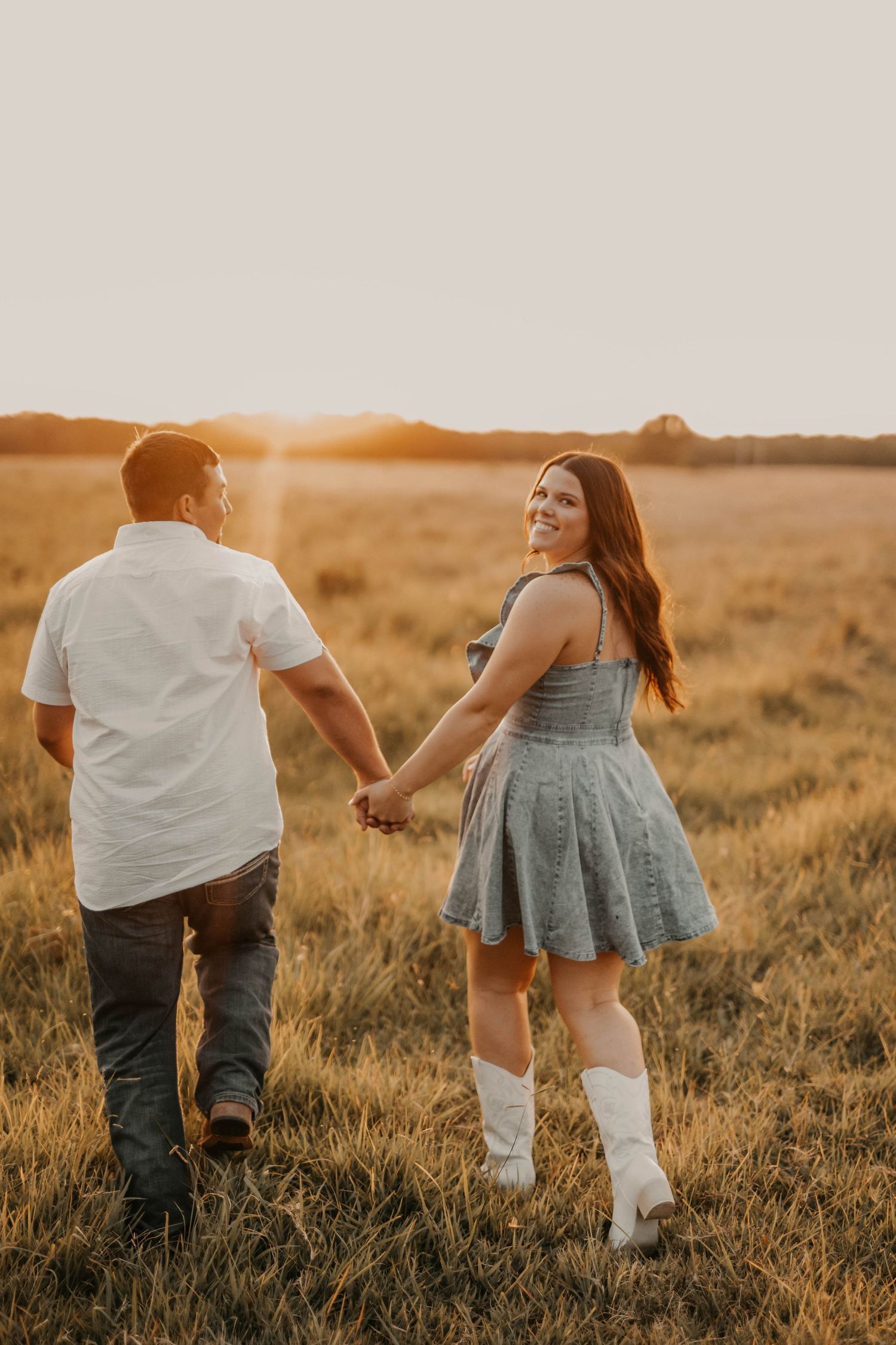 Couple holding hands while walking in golden field at sunset.