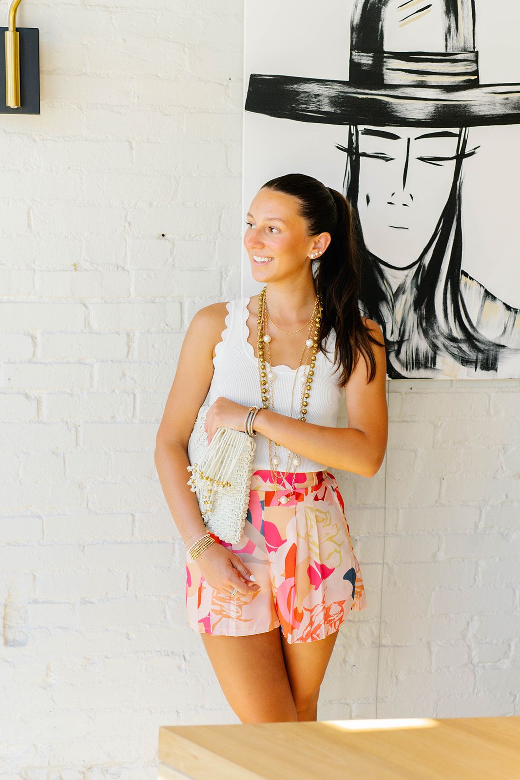 Woman in summer outfit poses against white wall with black art mural.