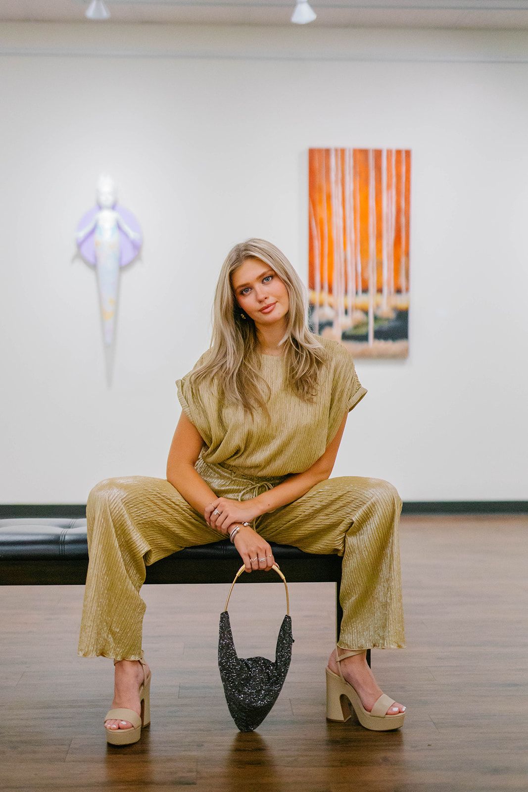 Fashion model in olive jumpsuit posing with handbag on hardwood floor.