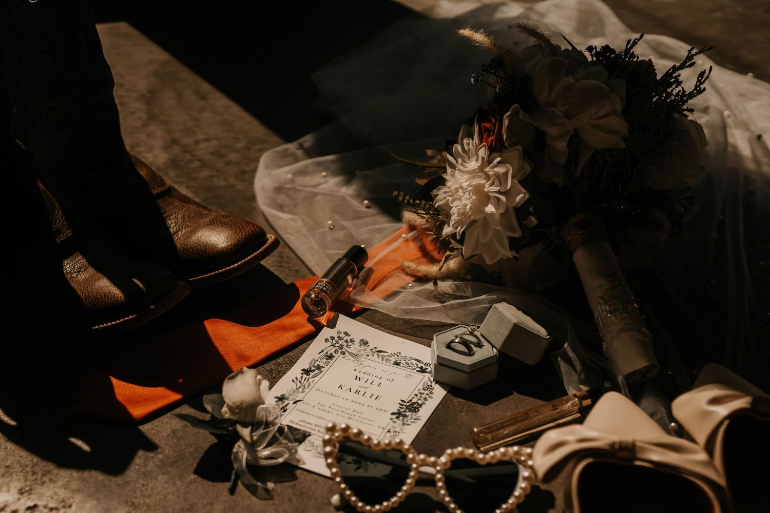 Wedding accessories including brown shoes, bow tie, and jewelry arranged with invitation cards.