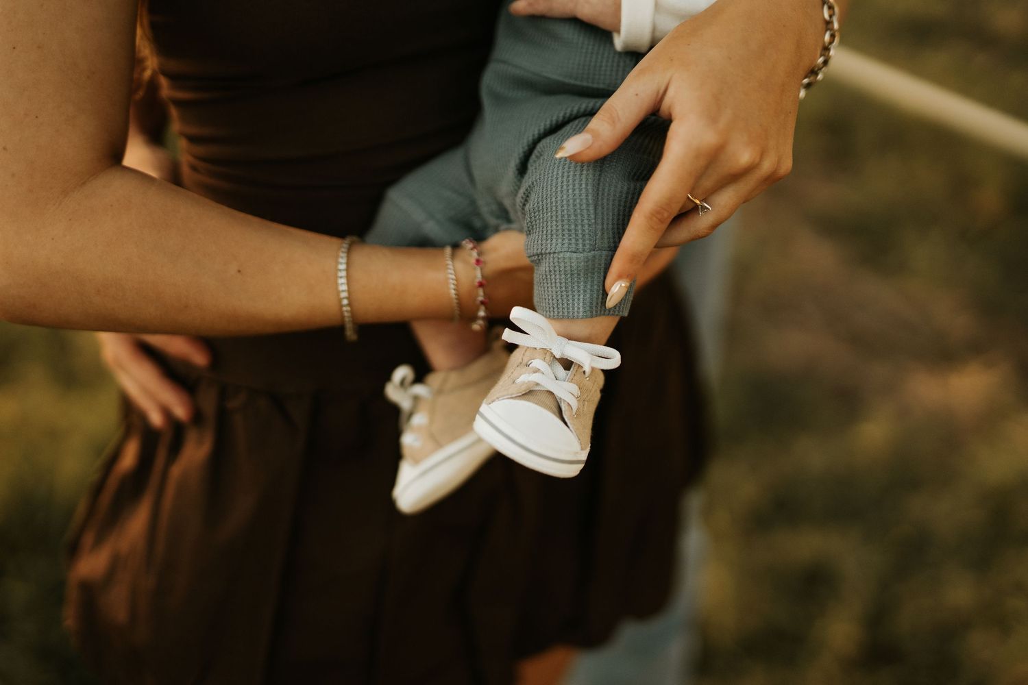 A mother holds her baby wearing tiny white sneakers outdoors in warm golden light.