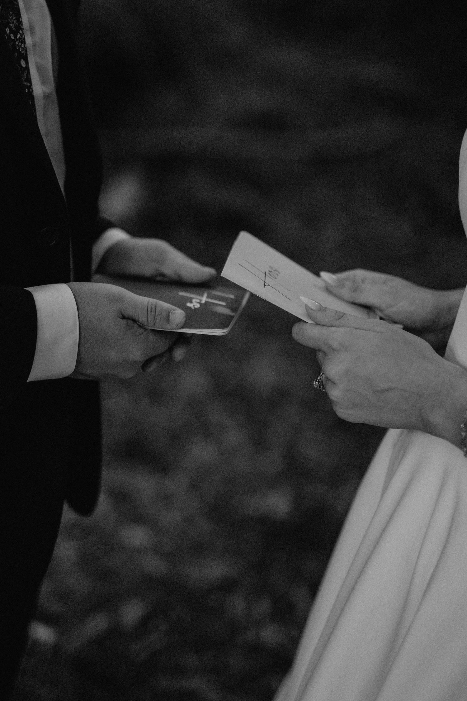 Black and white photo of hands exchanging wedding vows or letters.