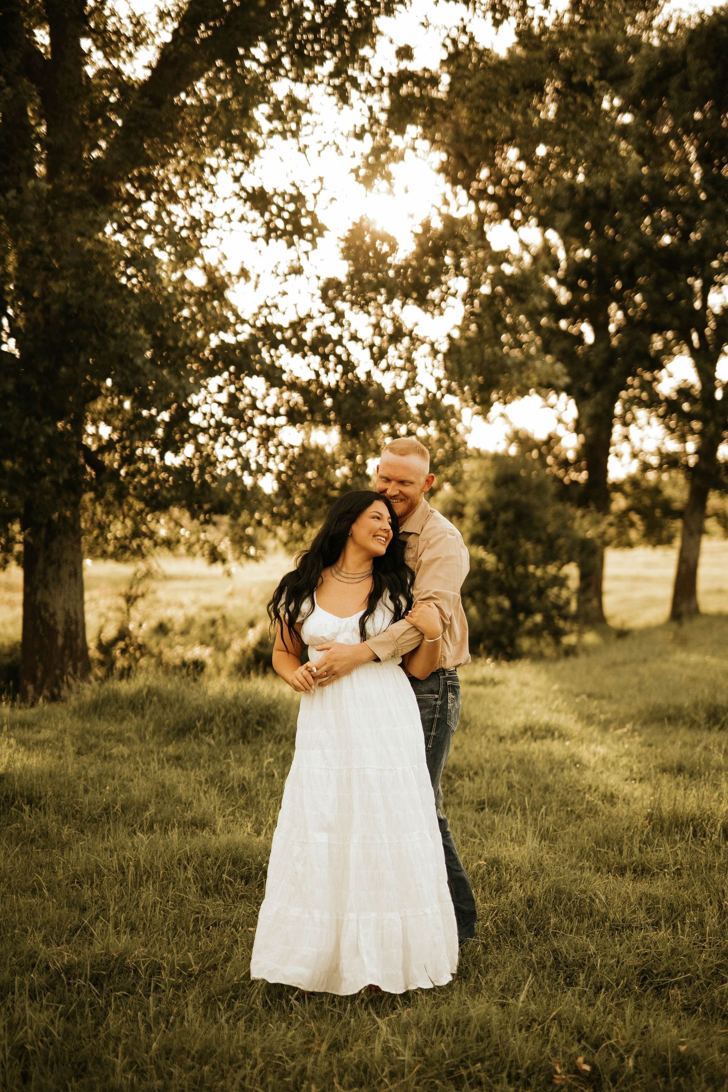 A couple shares a romantic moment in a white dress and casual attire against a golden sunset backdrop.