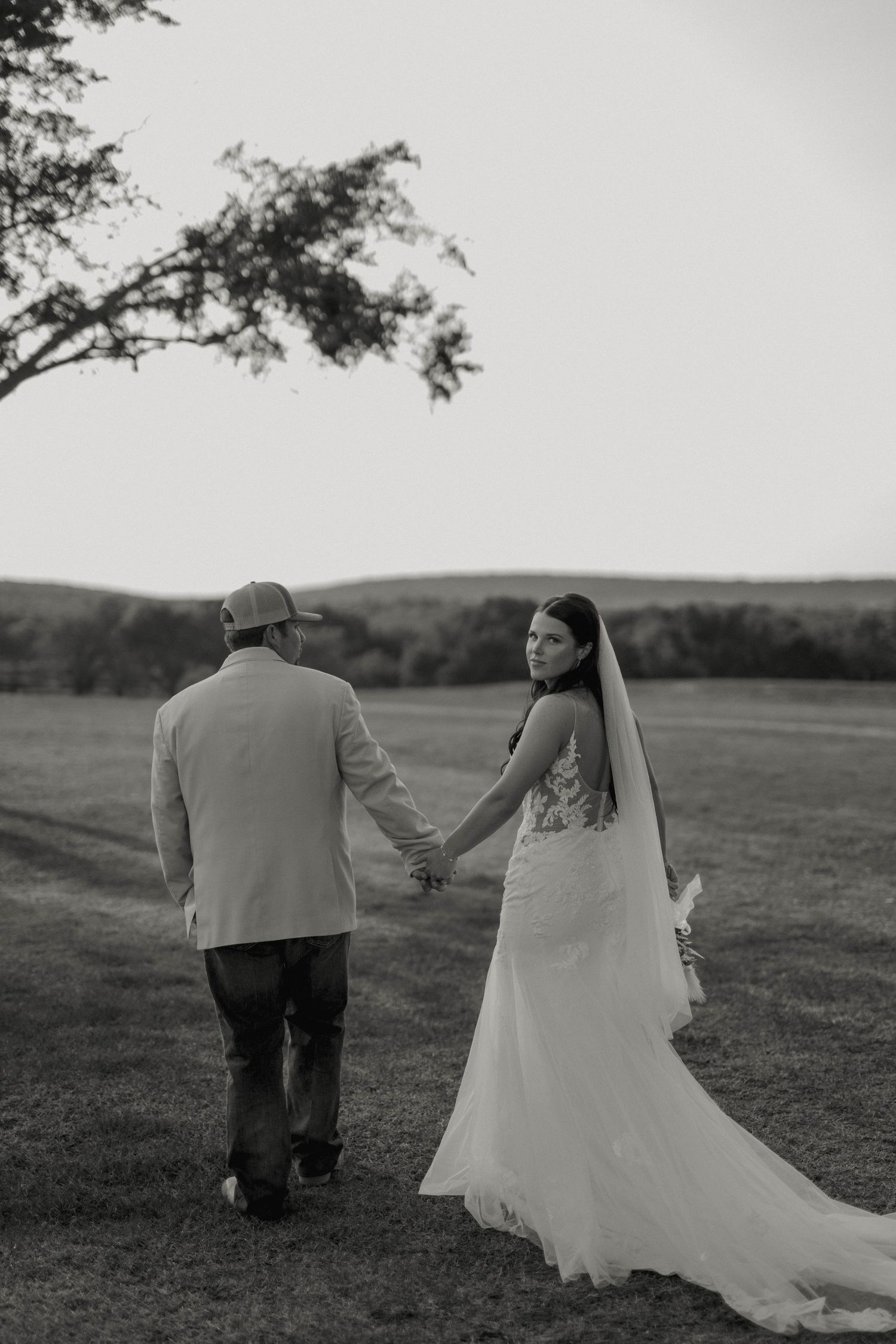 A couple walks hand in hand through a serene countryside setting.