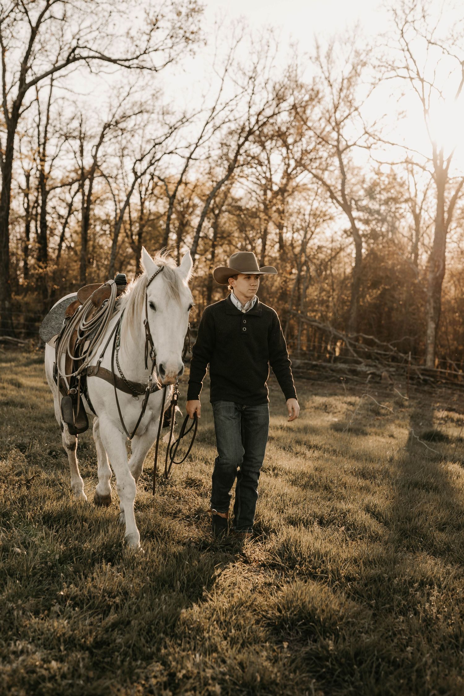 Person in black jacket walking alongside white horse in autumn forest setting.