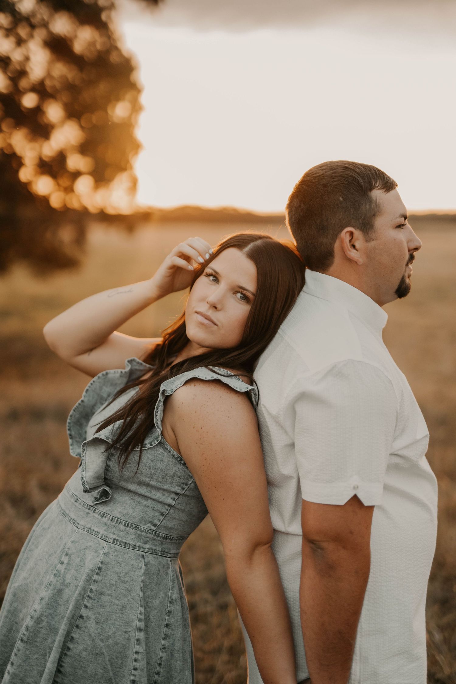 Playful couple posing back to back in field during golden hour photoshoot.