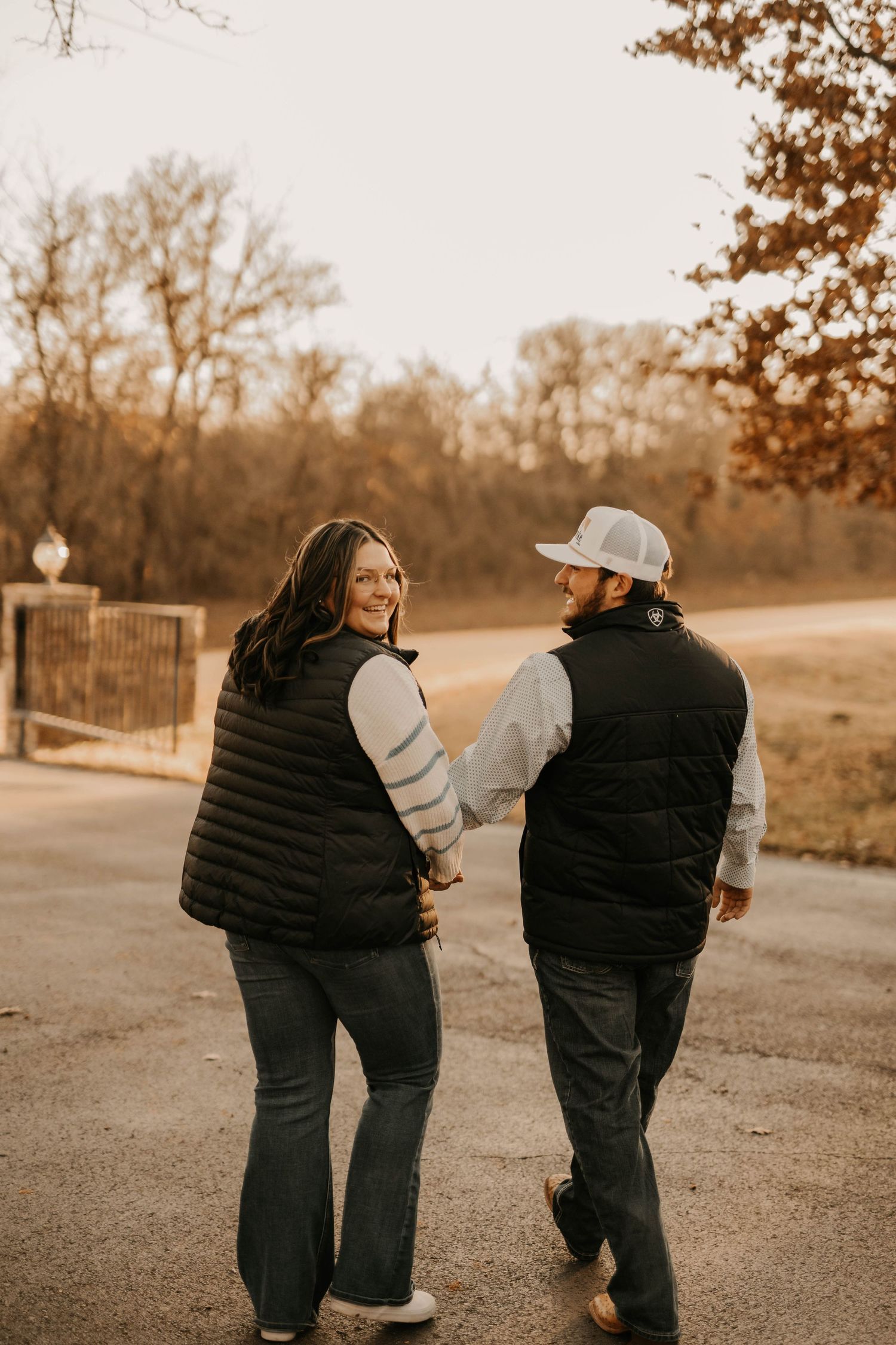 Happy couple walking hand in hand on path wearing matching black vests.