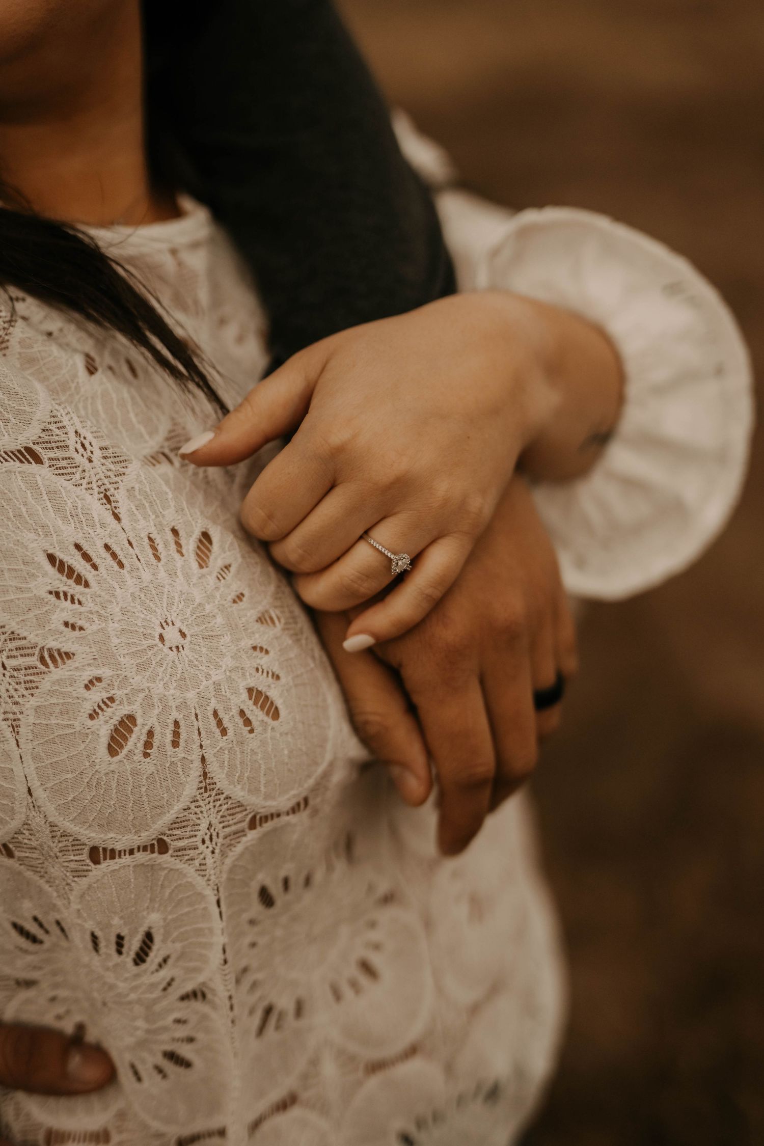 Close-up of hands resting on delicate white lace dress showing romantic details and textures.