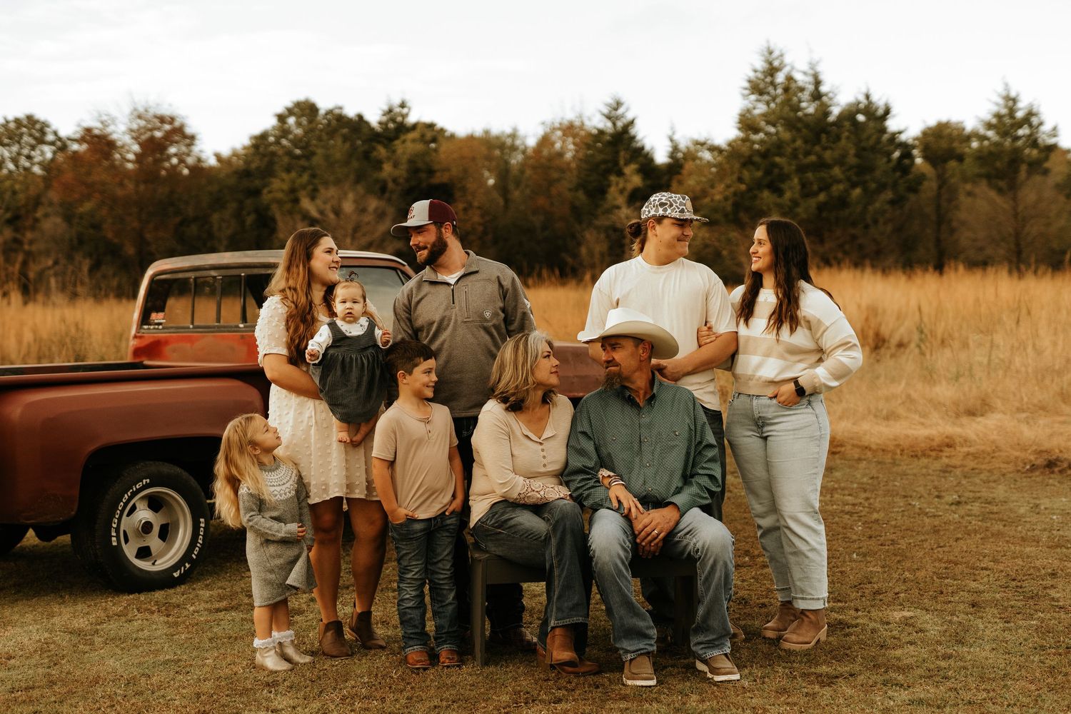 Multi-generational family posing together outdoors near a vintage red pickup truck in a rustic autumn field.
