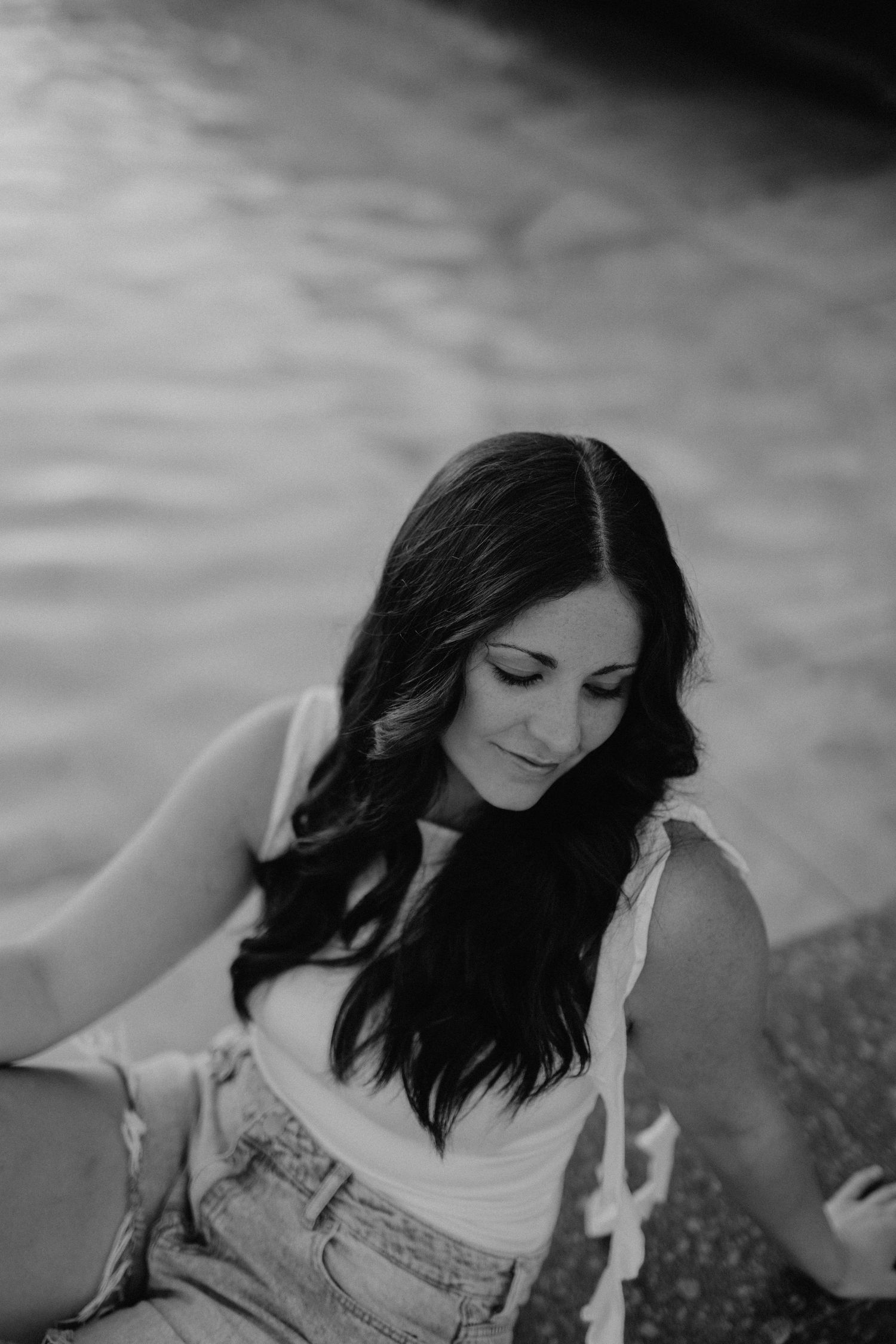 Black and white portrait of a woman in casual attire looking down with flowing dark hair.
