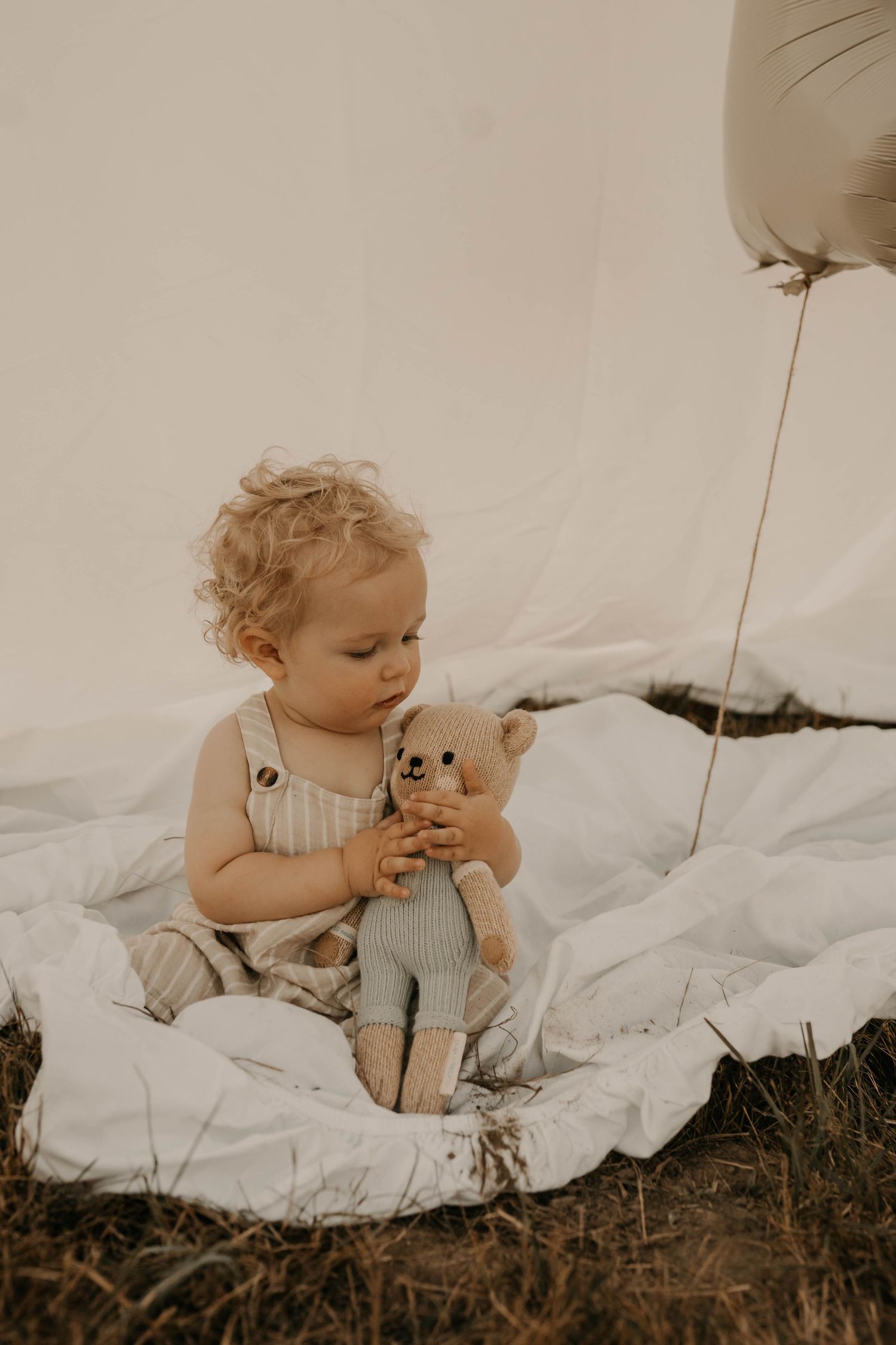 A baby plays on a white blanket in a field during a lifestyle photo session.