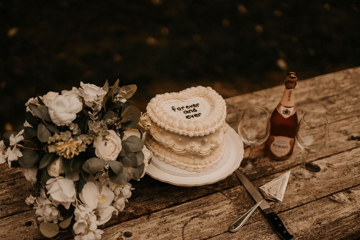 A rustic wedding setup with white flowers, a wedding cake, and champagne on a wooden surface.