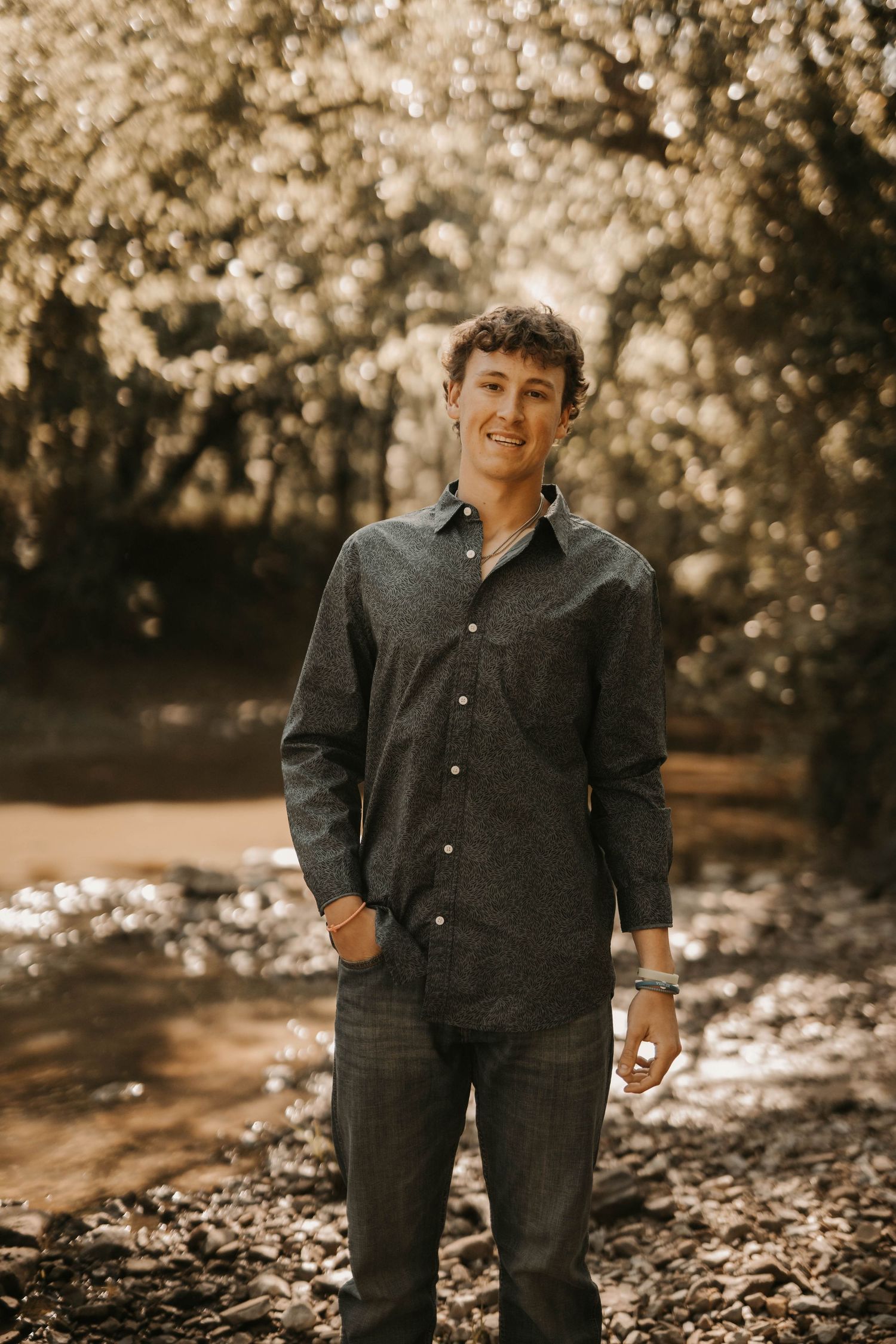 Casual portrait of someone in dark button-down shirt standing outdoors with autumn foliage background.