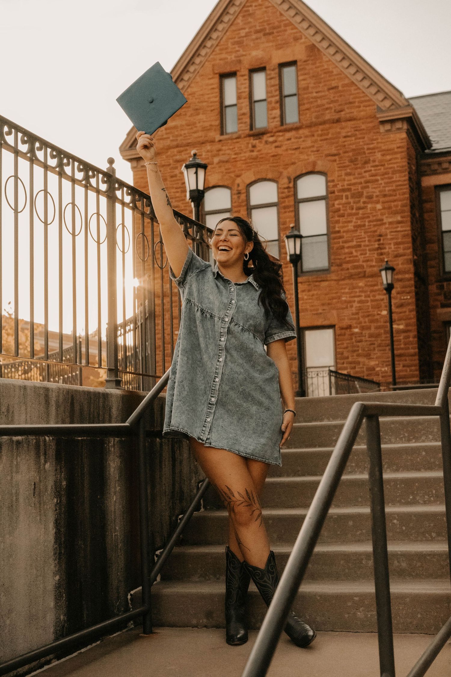 Graduate in denim dress celebrates by throwing cap on steps of brick building.