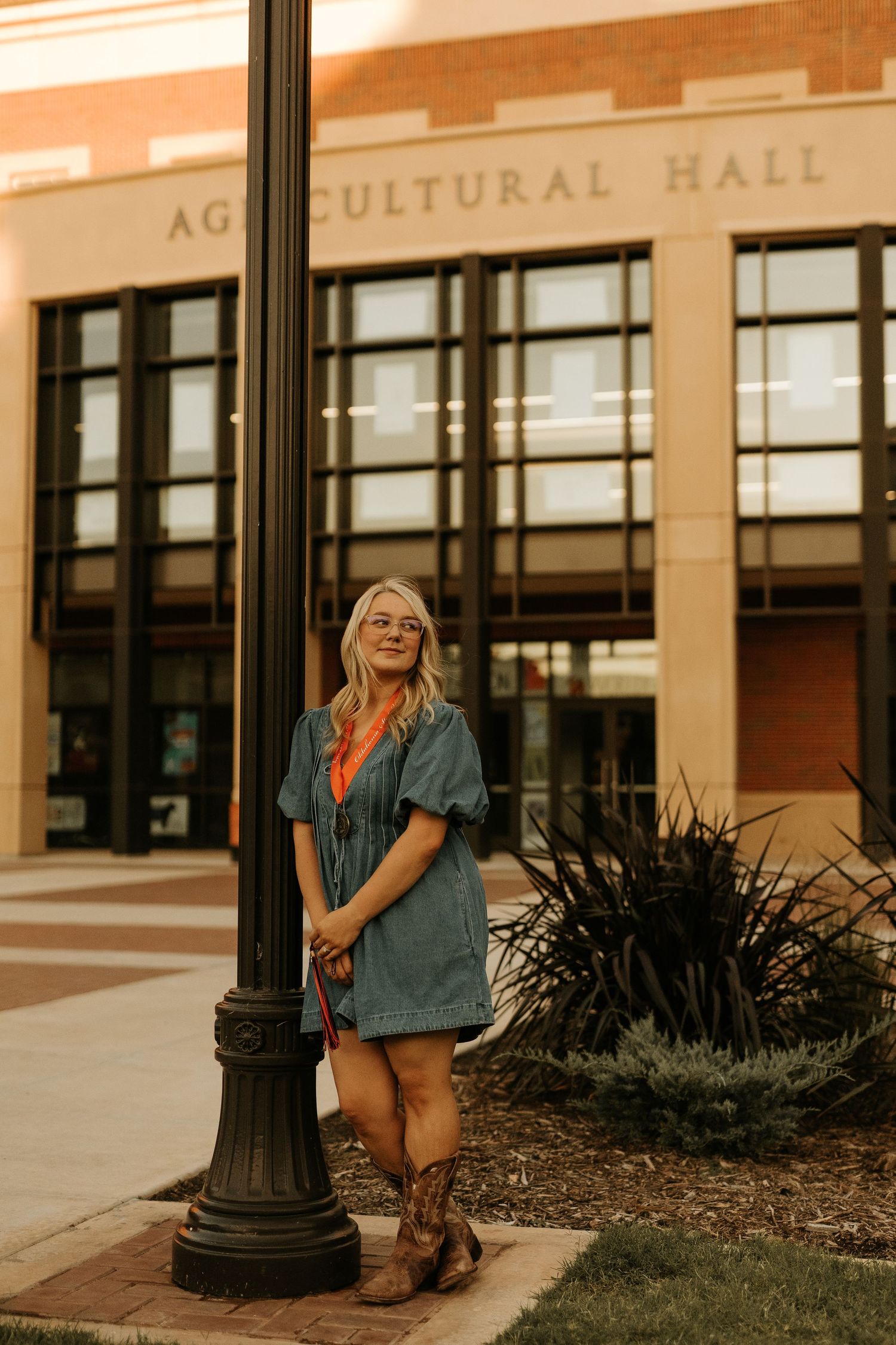 Blonde woman in denim dress and cowboy boots posing by a lamppost outside Agricultural Hall.