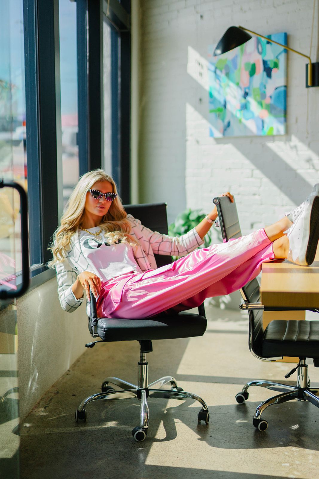 Casual office setting with relaxed pose in pink loungewear and sunglasses.