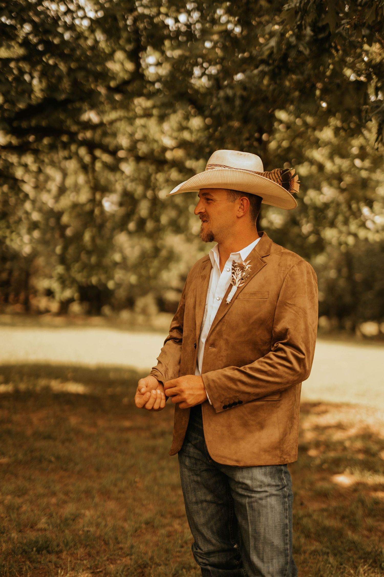 A person in western wear and cowboy hat smiles in warm afternoon sunlight.
