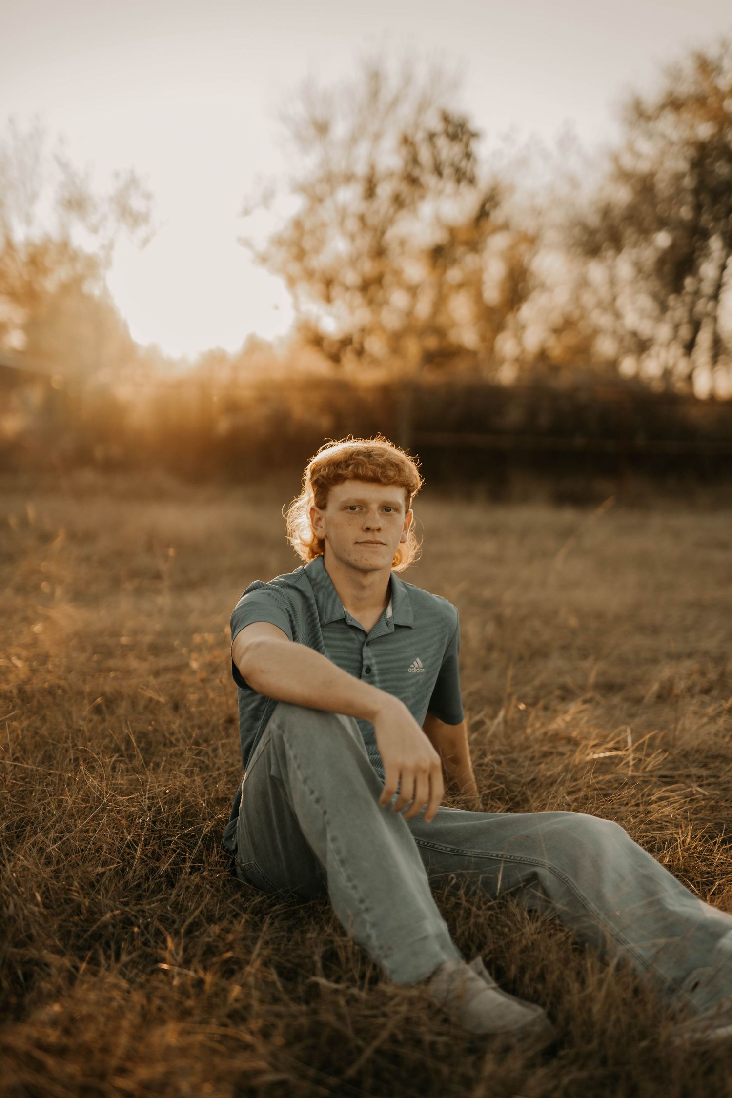 Person in polo shirt sits casually in field during sunset with golden light.