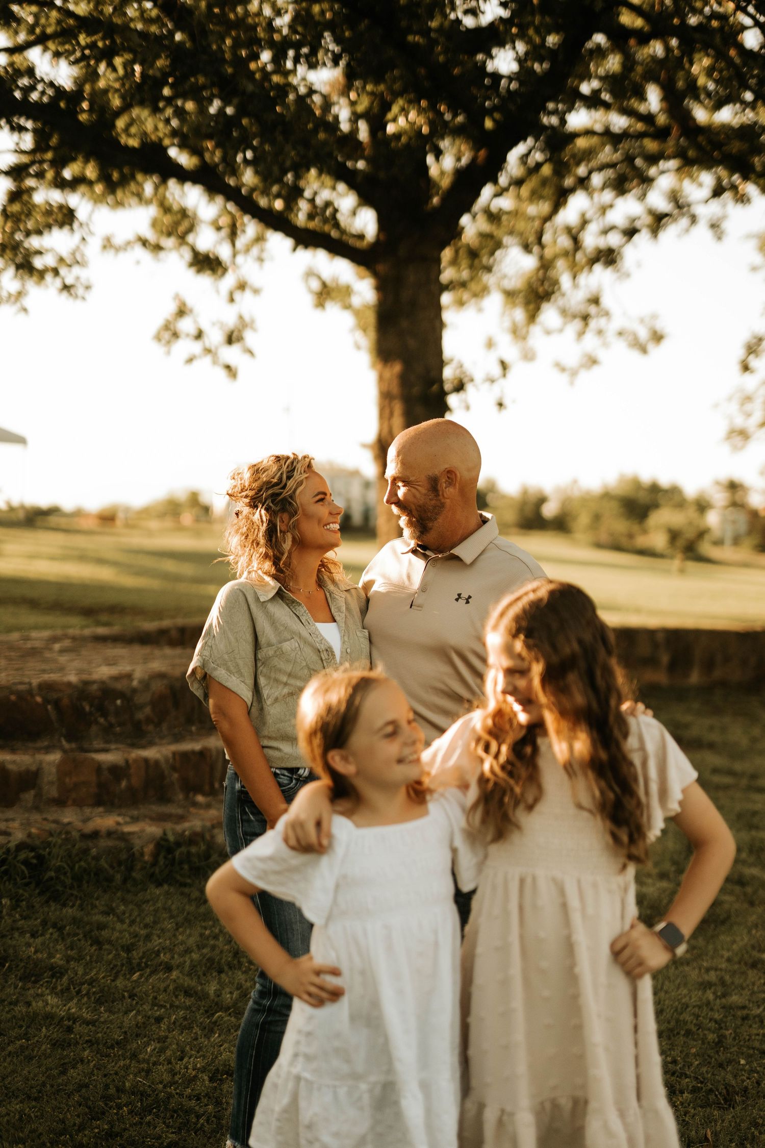 A family of four poses together during golden hour under a large tree.