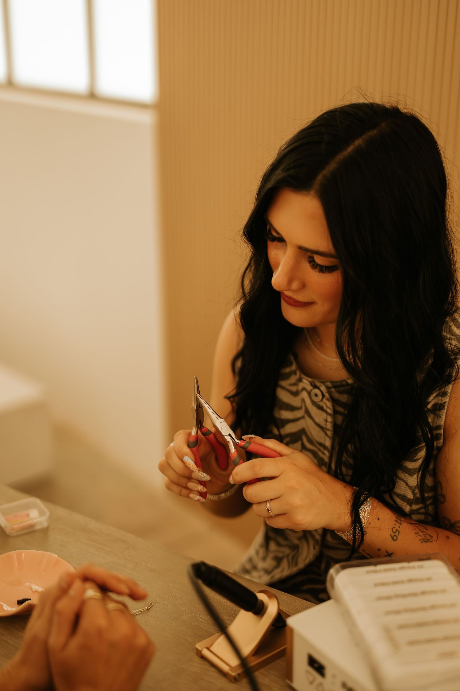 Dark-haired woman applying press-on nails at a beauty salon table with tools and accessories.