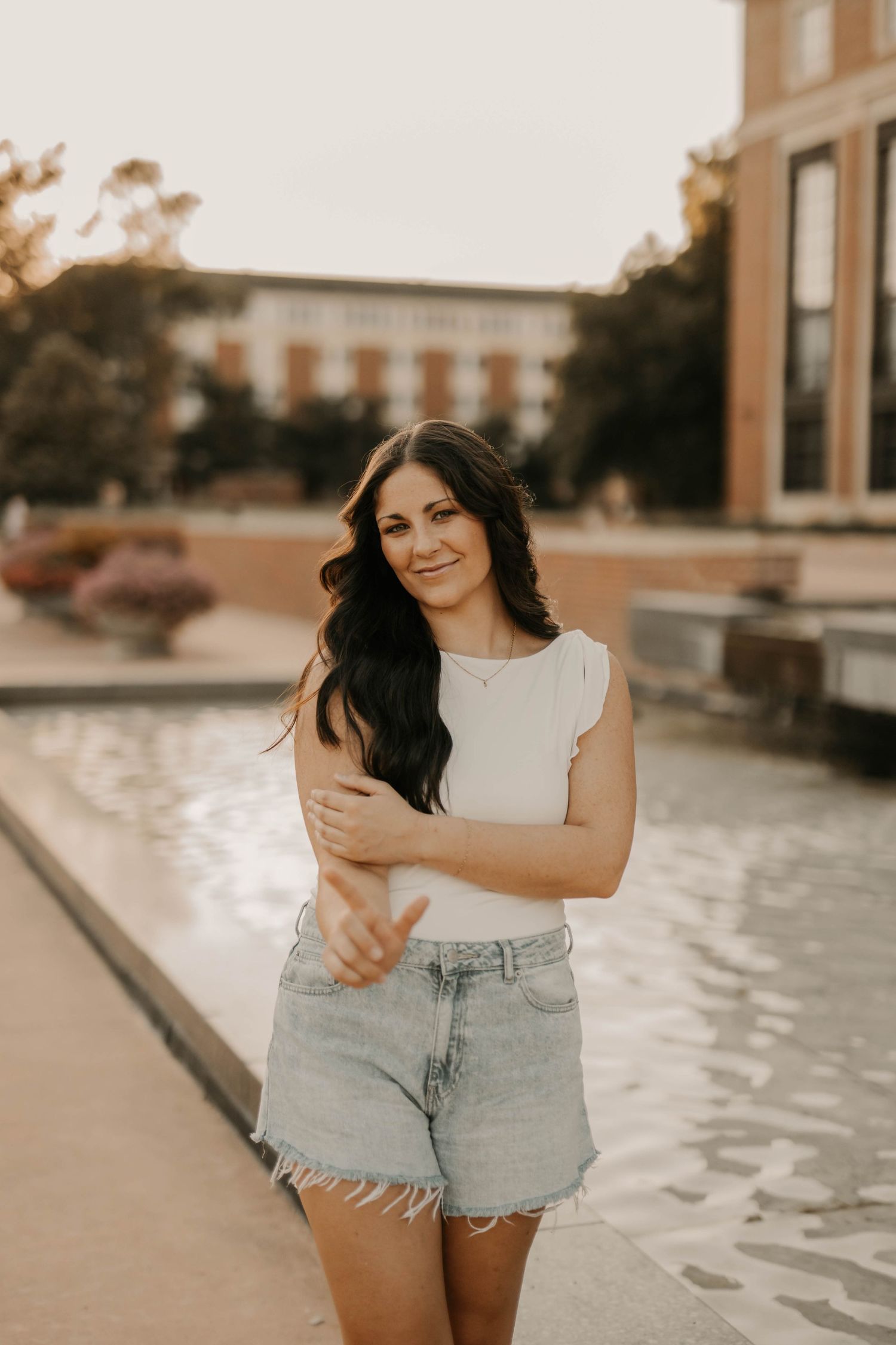 A person in casual attire poses against an architectural backdrop during sunset.