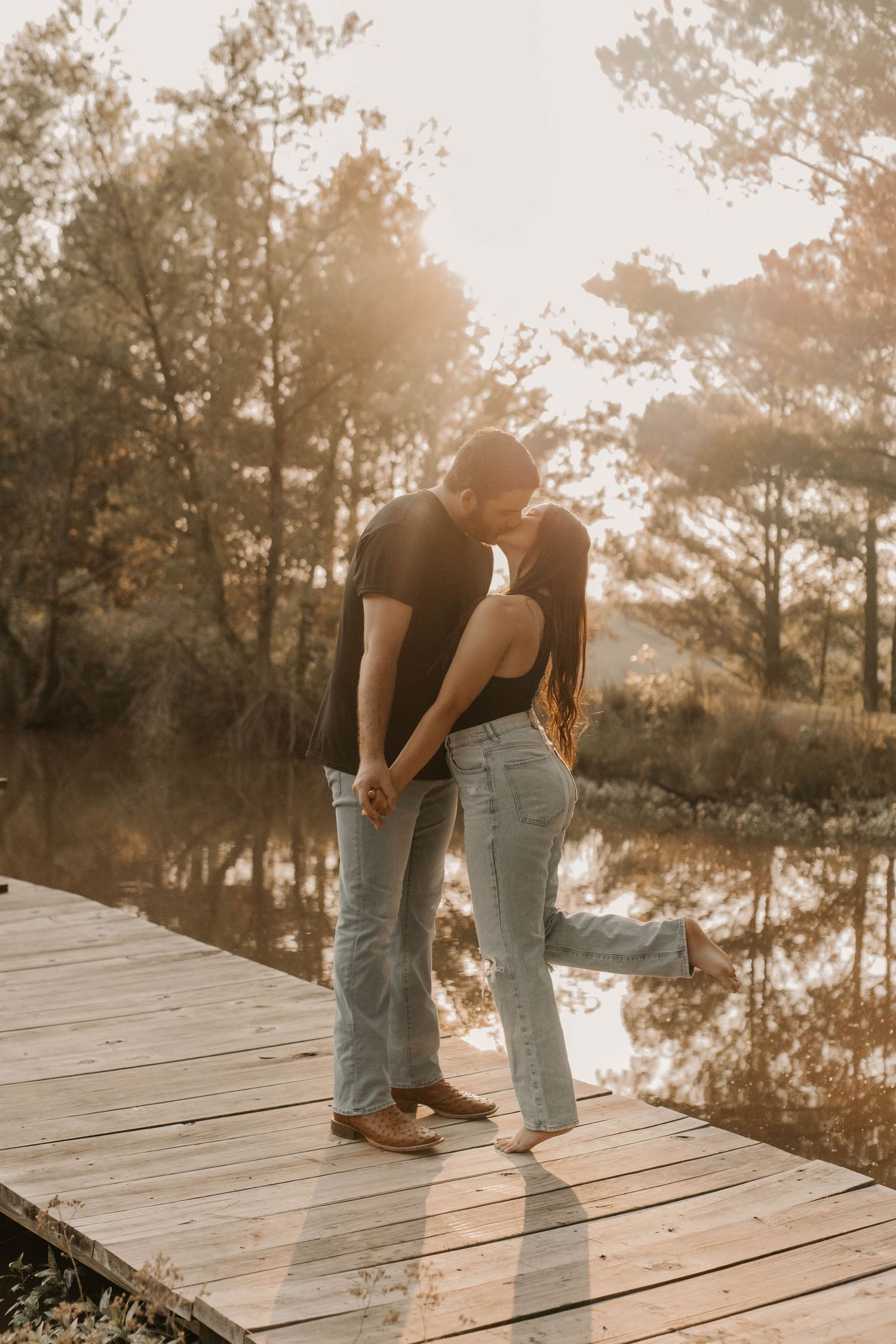 Romantic couple sharing an intimate moment on a wooden dock during golden hour by a tranquil lake.