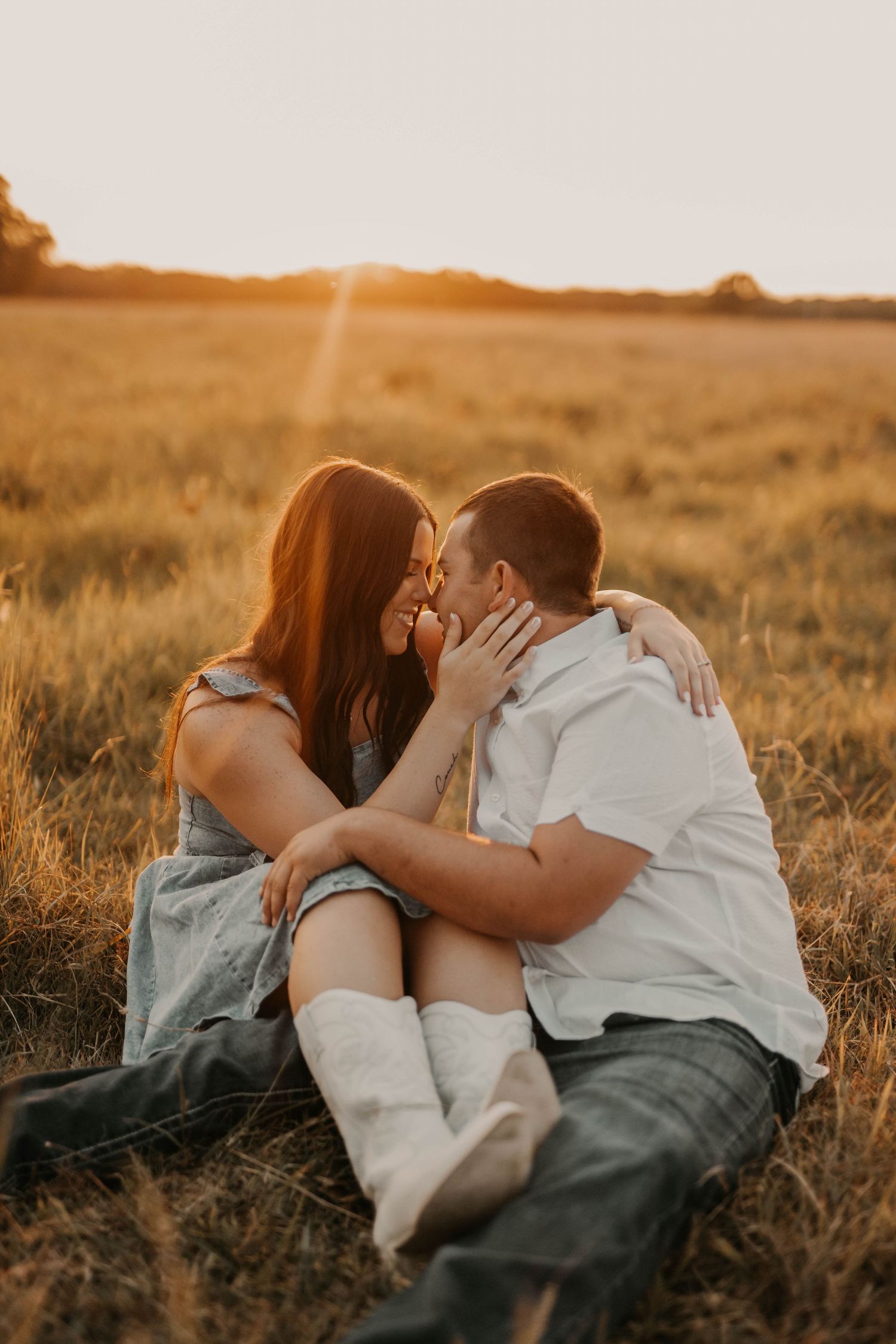 Intimate couple sitting in golden field sharing romantic moment at sunset.