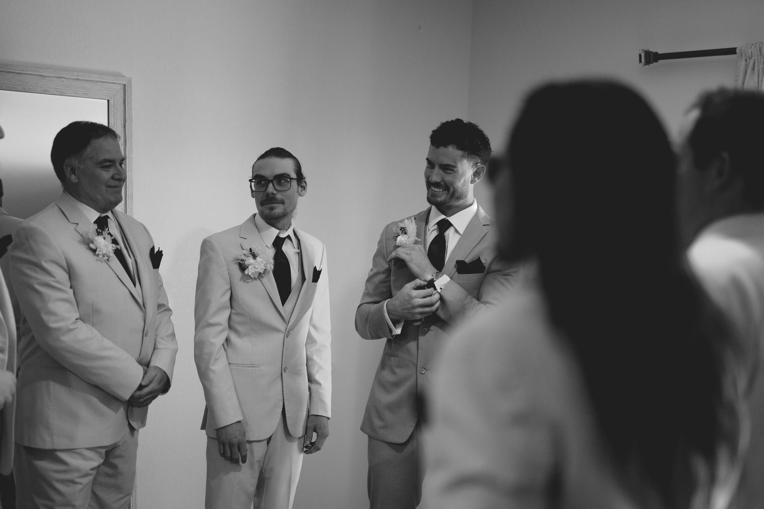 Black and white photo of groomsmen in light suits laughing and talking before a wedding ceremony.
