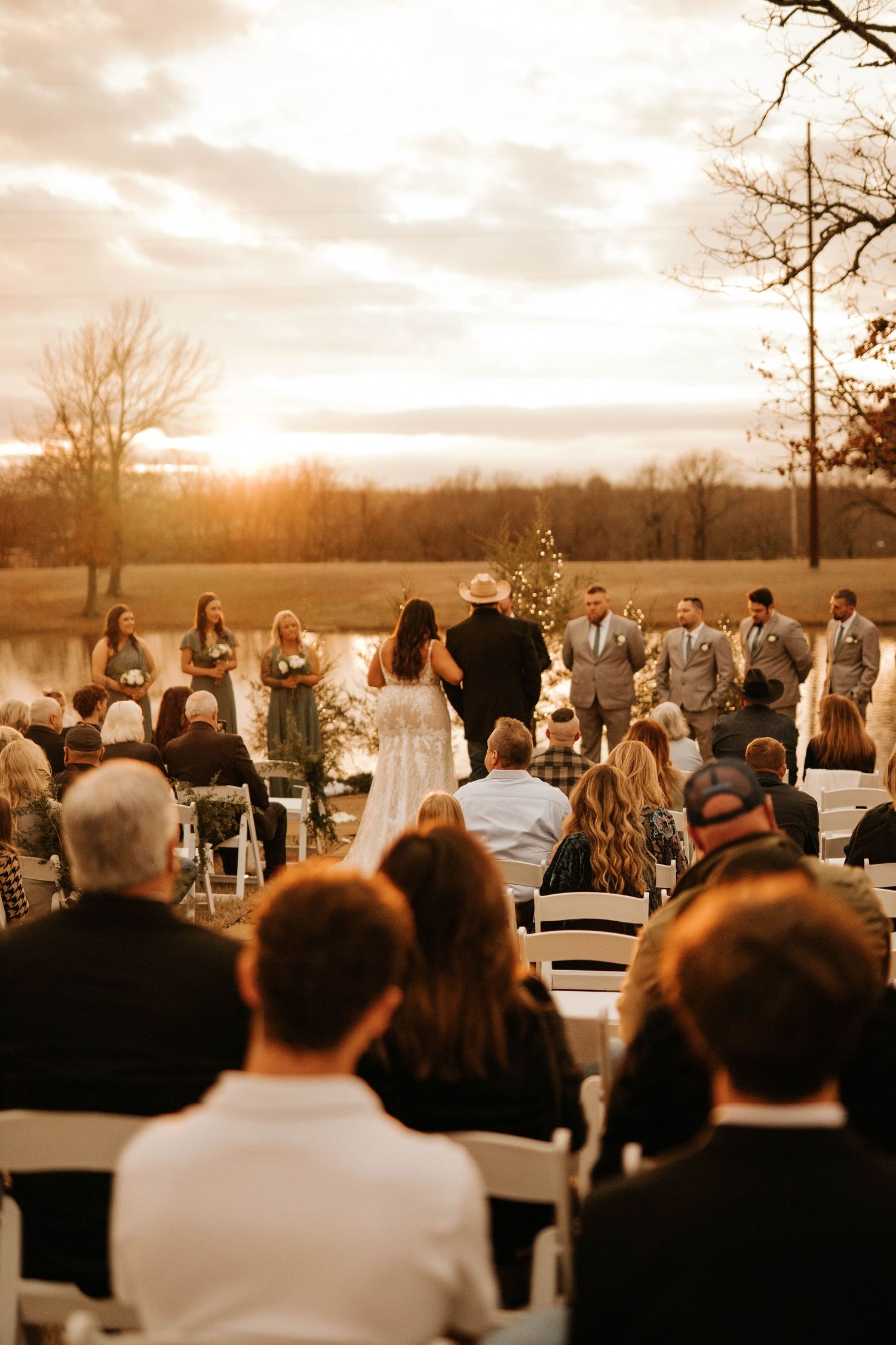 Outdoor sunset wedding ceremony with guests seated facing couple against golden sky backdrop.