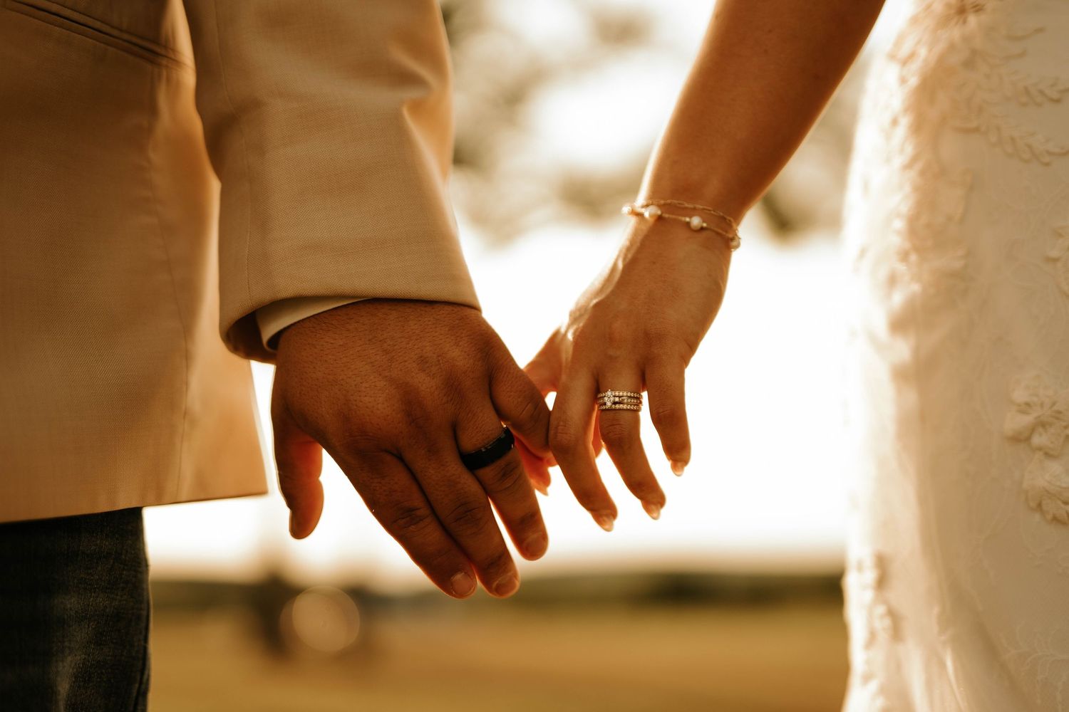 Two hands reaching for each other wearing wedding rings in golden sunlight.