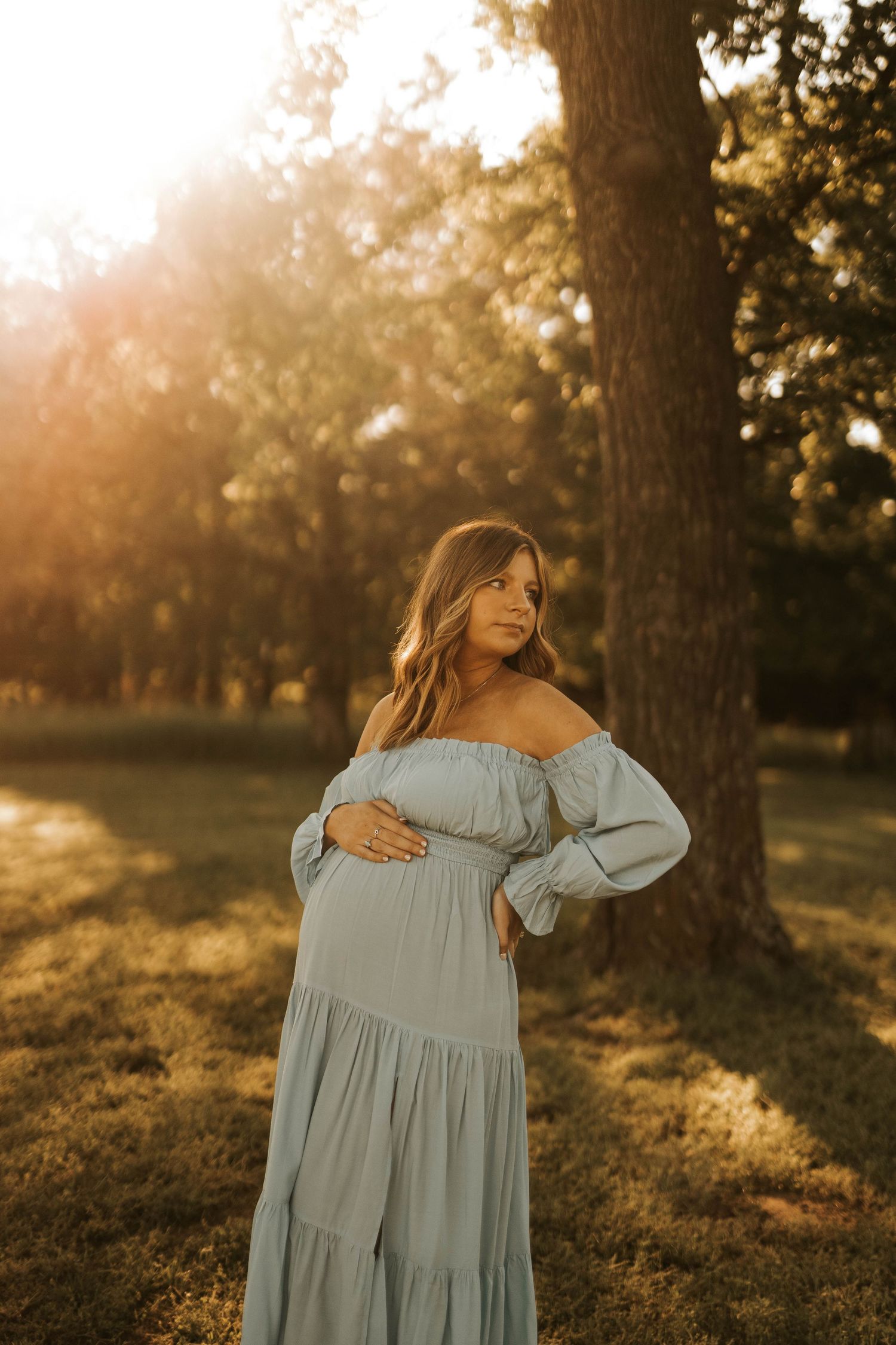 Maternity photos in a park at golden hour showing a flowing light blue dress.