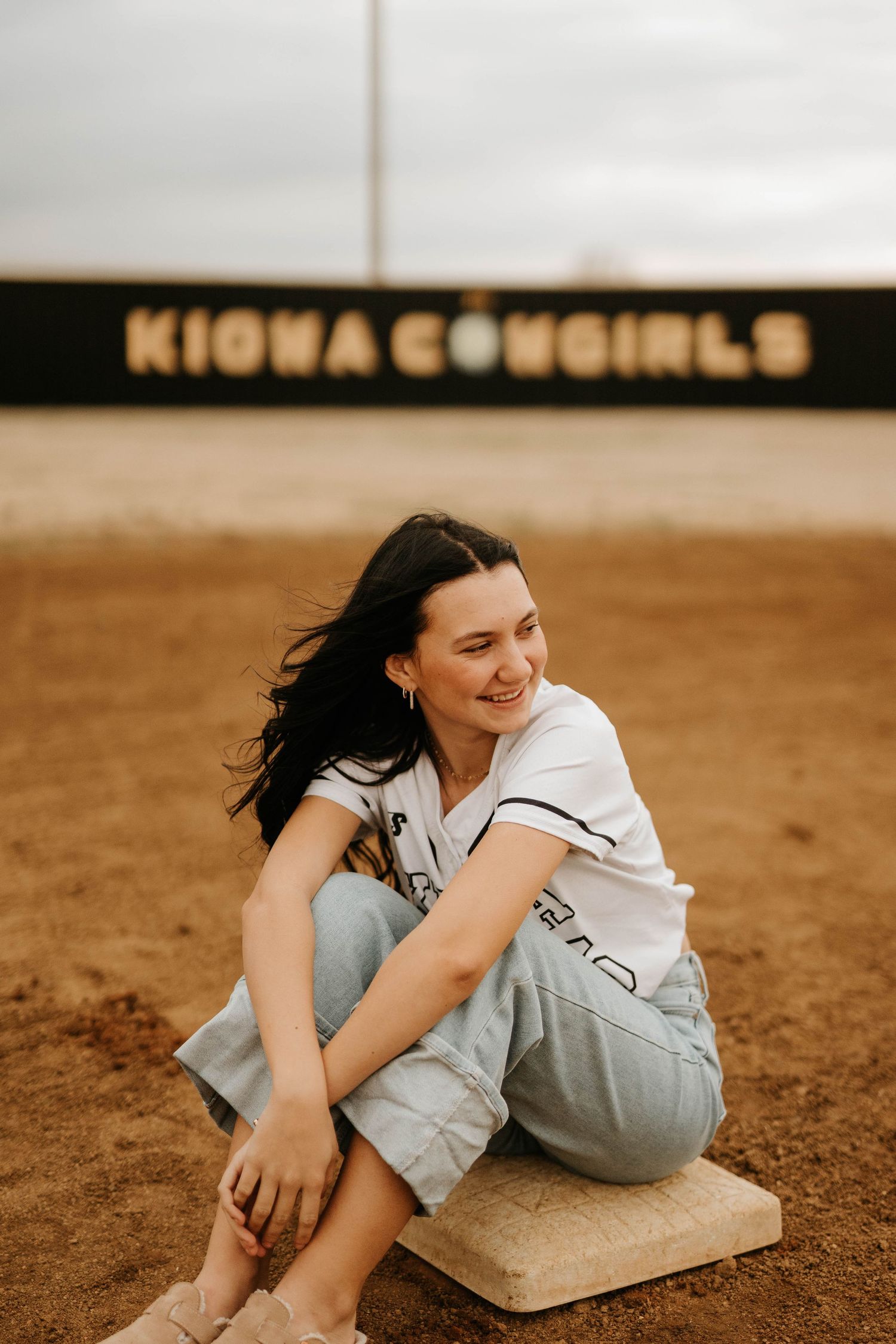 Person in casual attire sits on ground beneath Kiowa Cowgirls sign with warm lighting.
