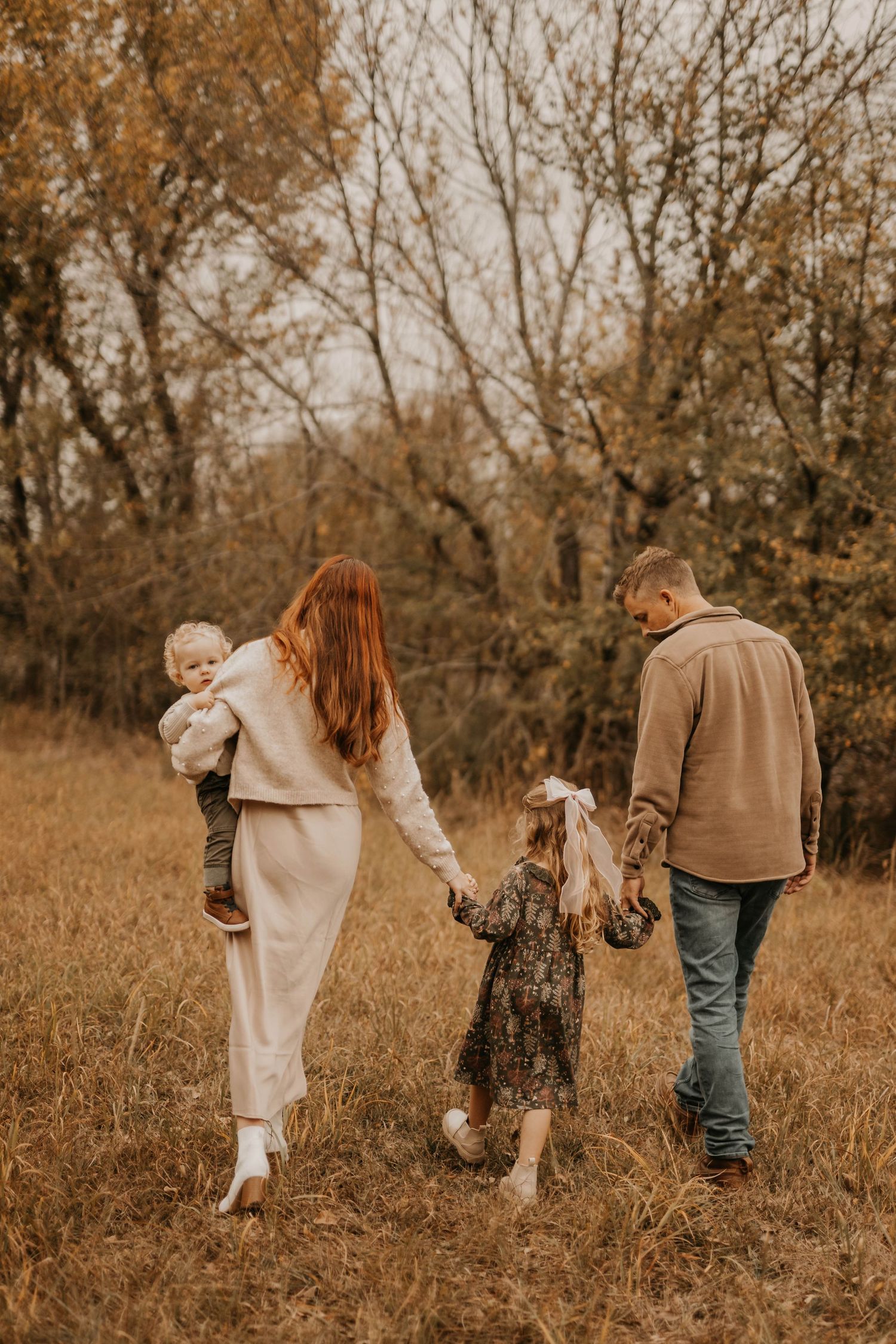 Family walking together through golden grass field on autumn afternoon.