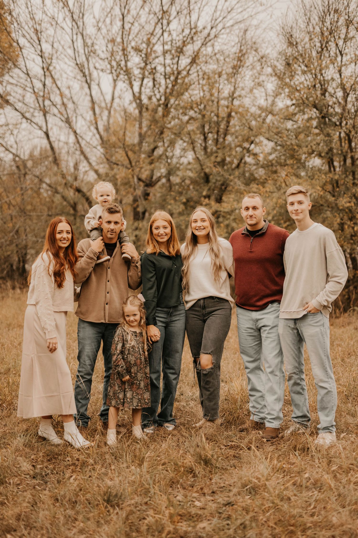 Extended family group photo in coordinated neutral outfits against autumn forest backdrop.