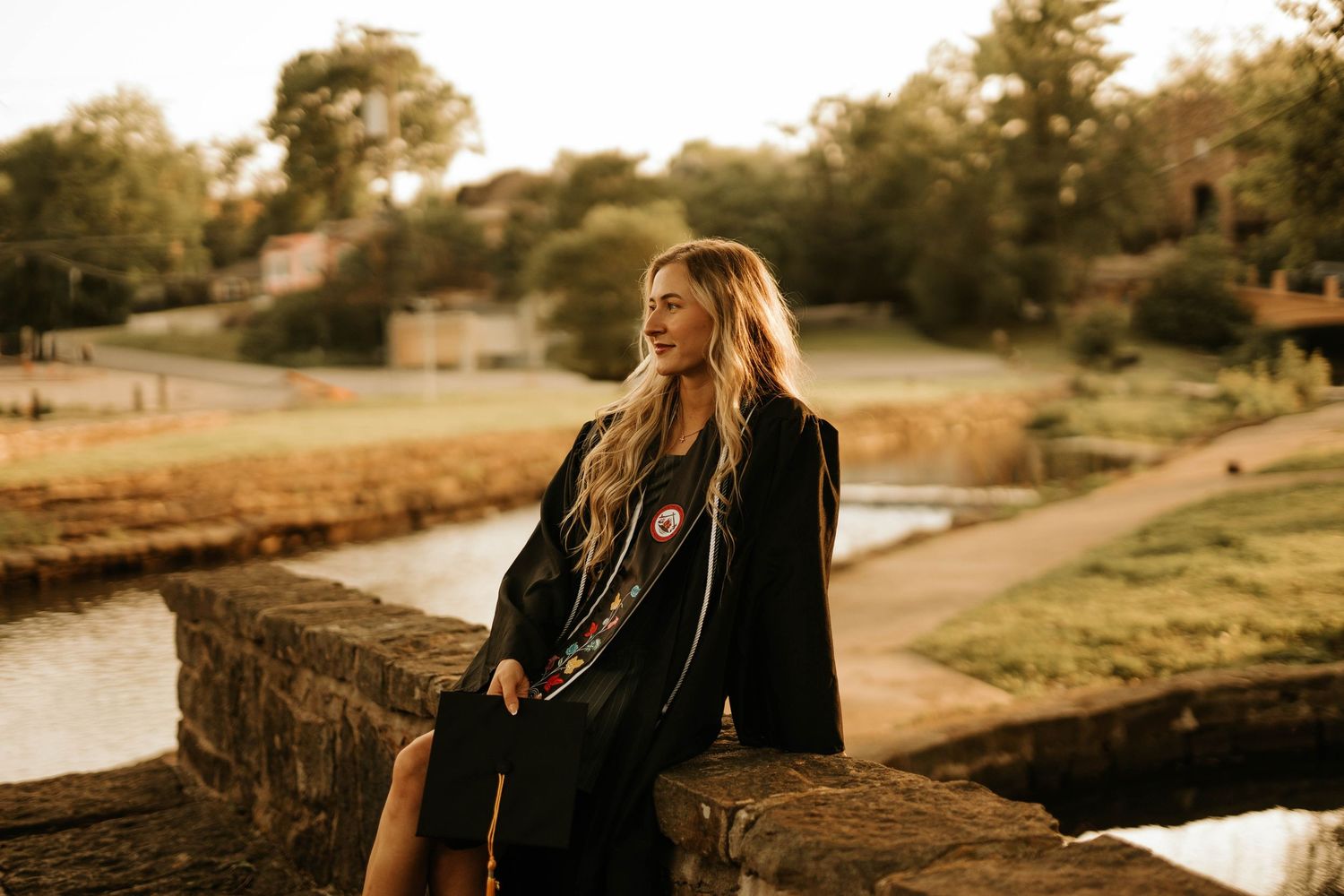 A person in black sits on a stone wall near a river at golden hour.