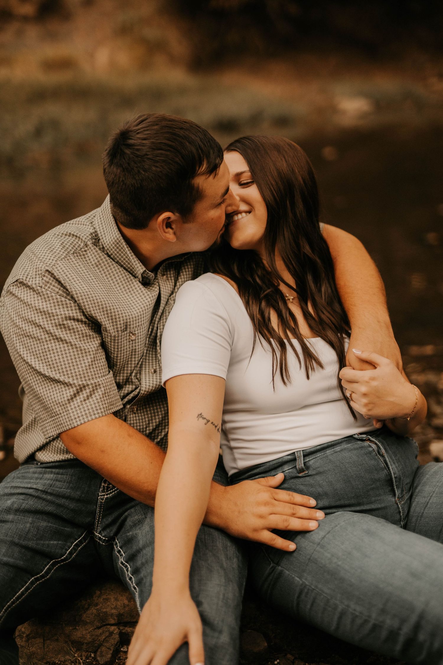 Intimate moment between couple sitting on rocks by water during sunset.