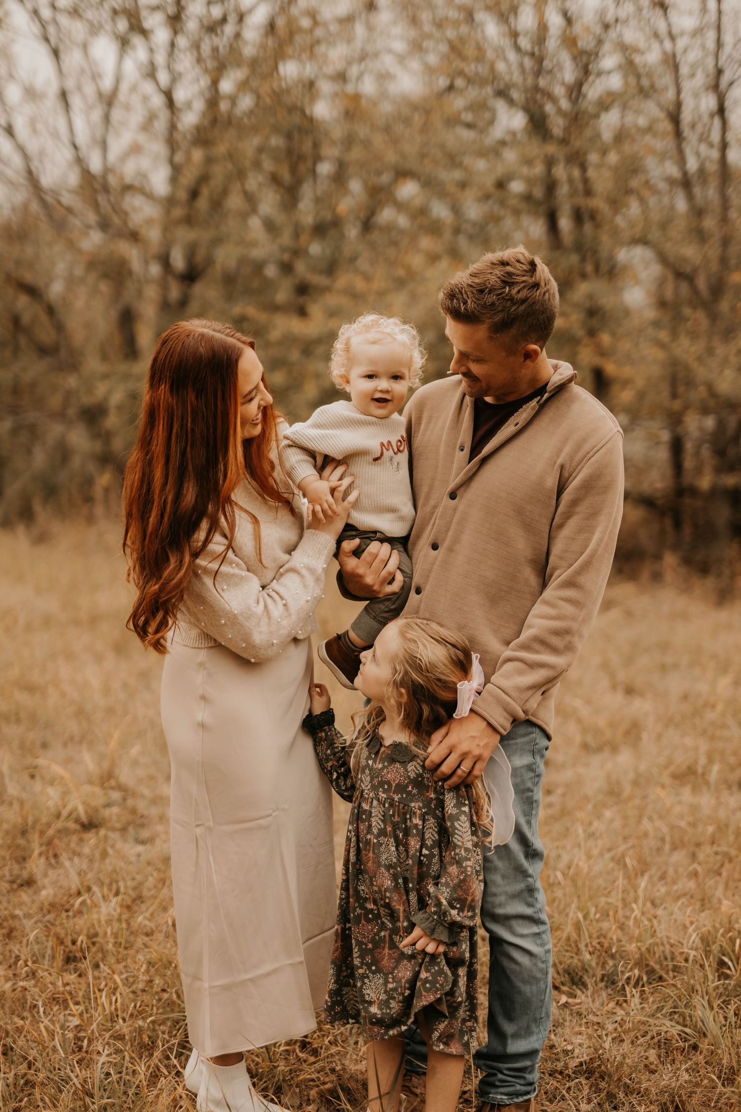 Family in neutral tones sharing tender moment together in autumn field.
