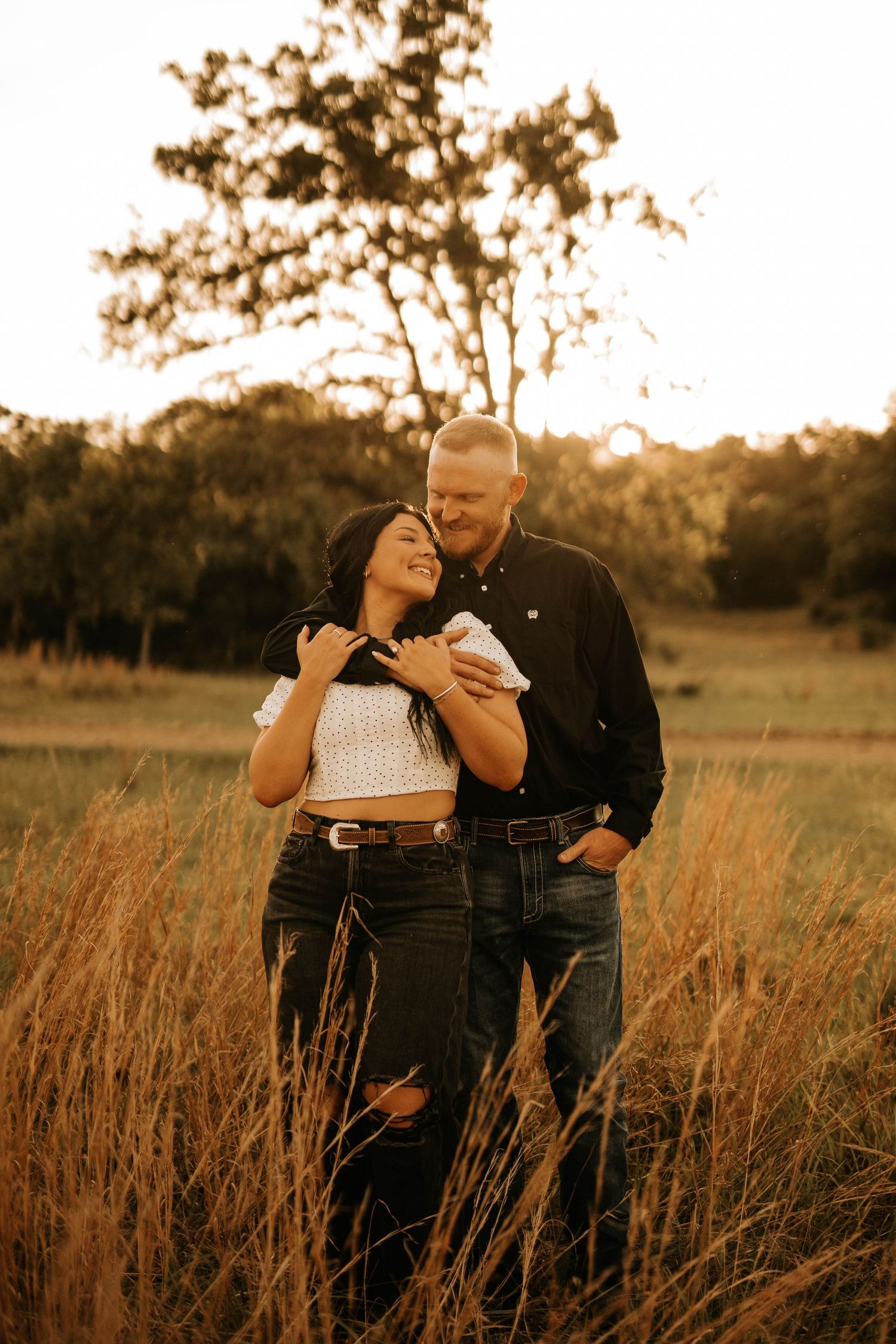 Couple sharing a loving moment in casual attire against a warm sunset in tall grass.