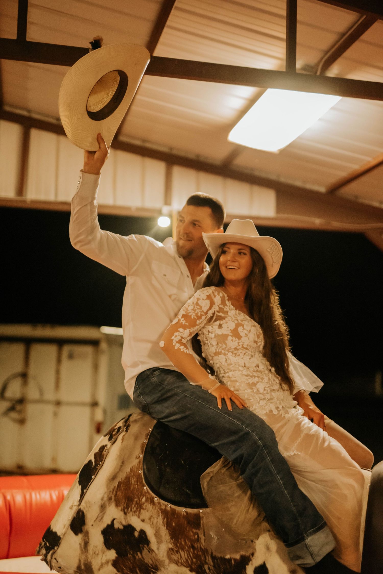 A couple in western attire poses on a mechanical bull at their reception.