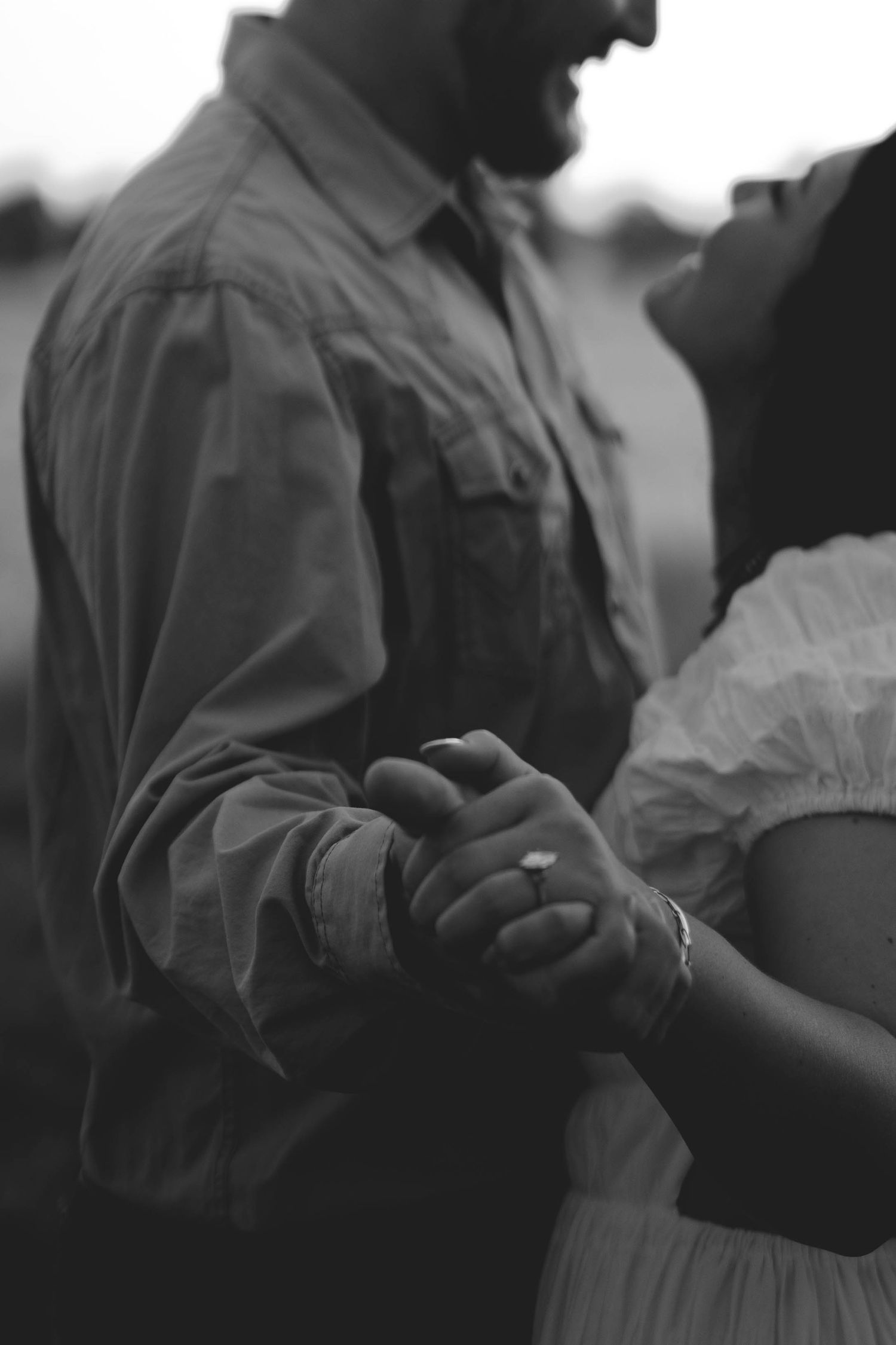 Black and white close-up of a couple holding hands while dancing outdoors.
