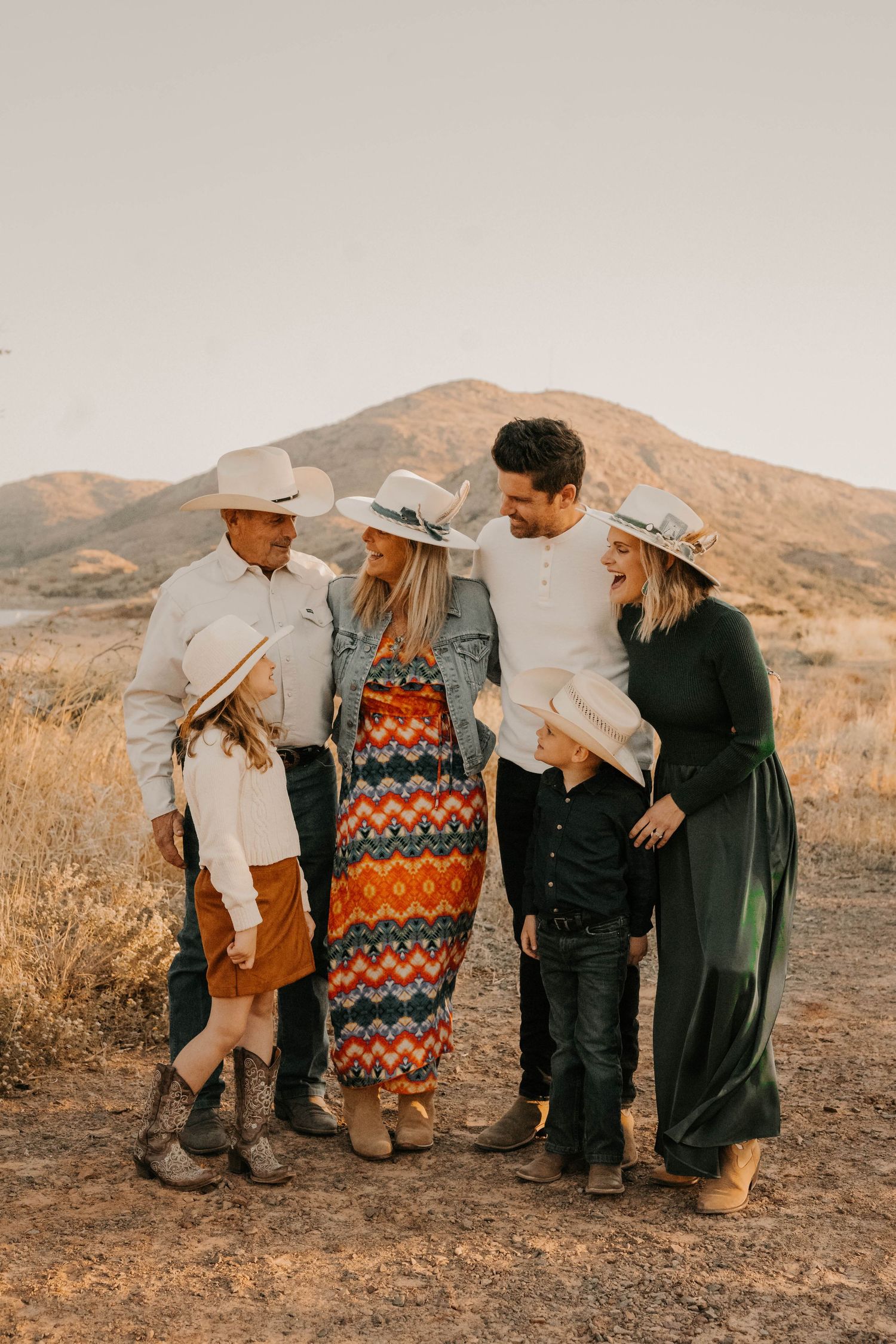 Group of friends laughing together in casual fall outfits against desert mountain backdrop at sunset.