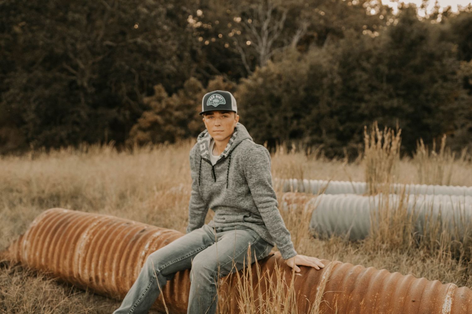 Person in casual wear sitting on industrial pipe in rural setting.